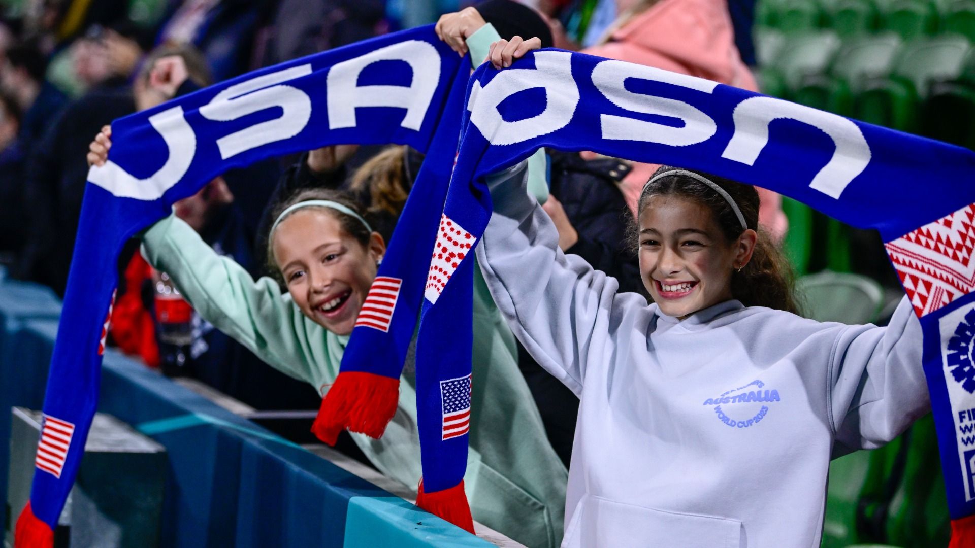 Young USWNT fans smiling and holding "USA" scarves during a game between Sweden and USWNT at Melbourne Rectangular Stadium on August 6, 2023 in Australia. 