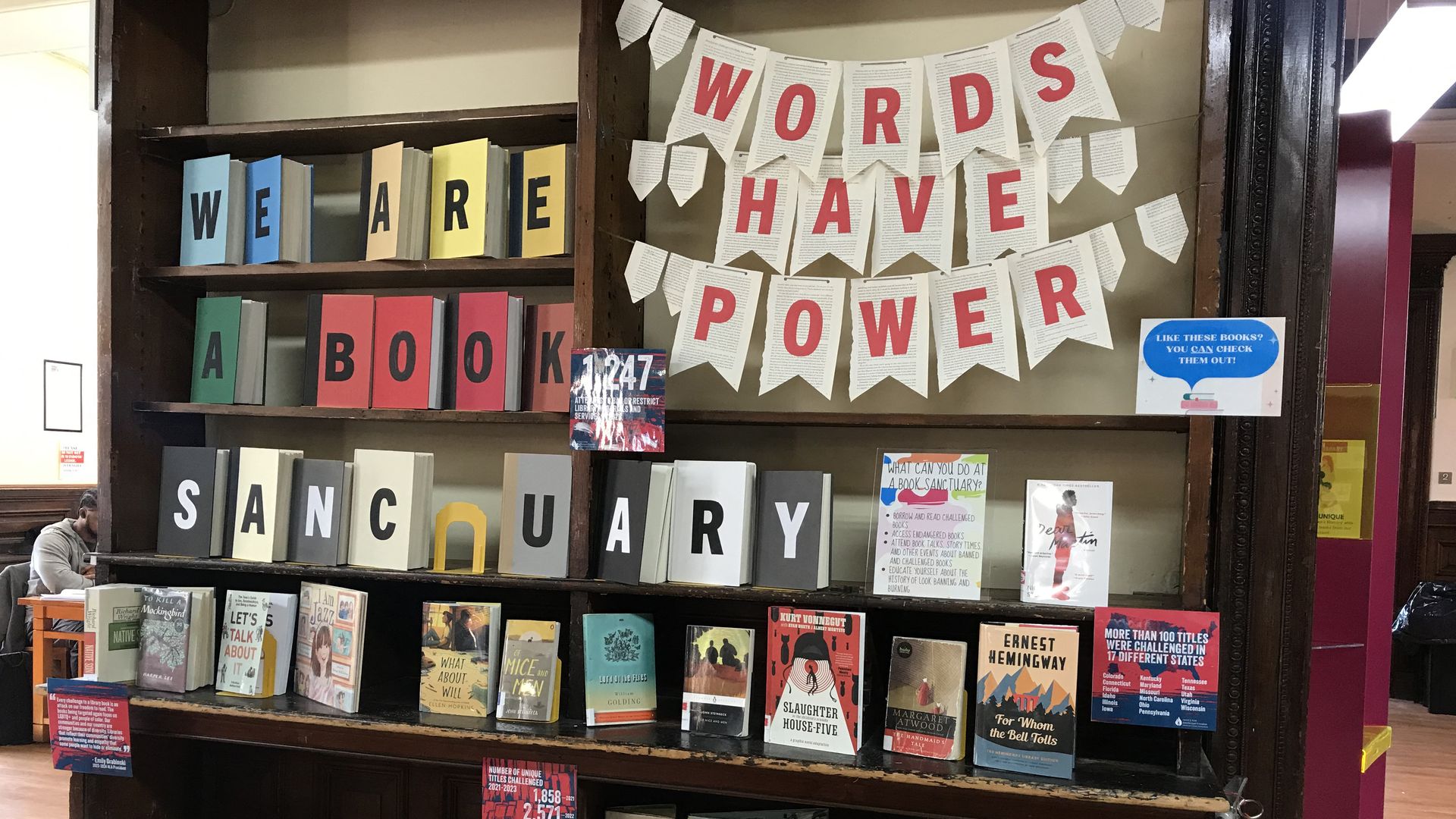 A library book stack featuring the phrases "Words Have Power" and "We Are A Book Sanctuary."