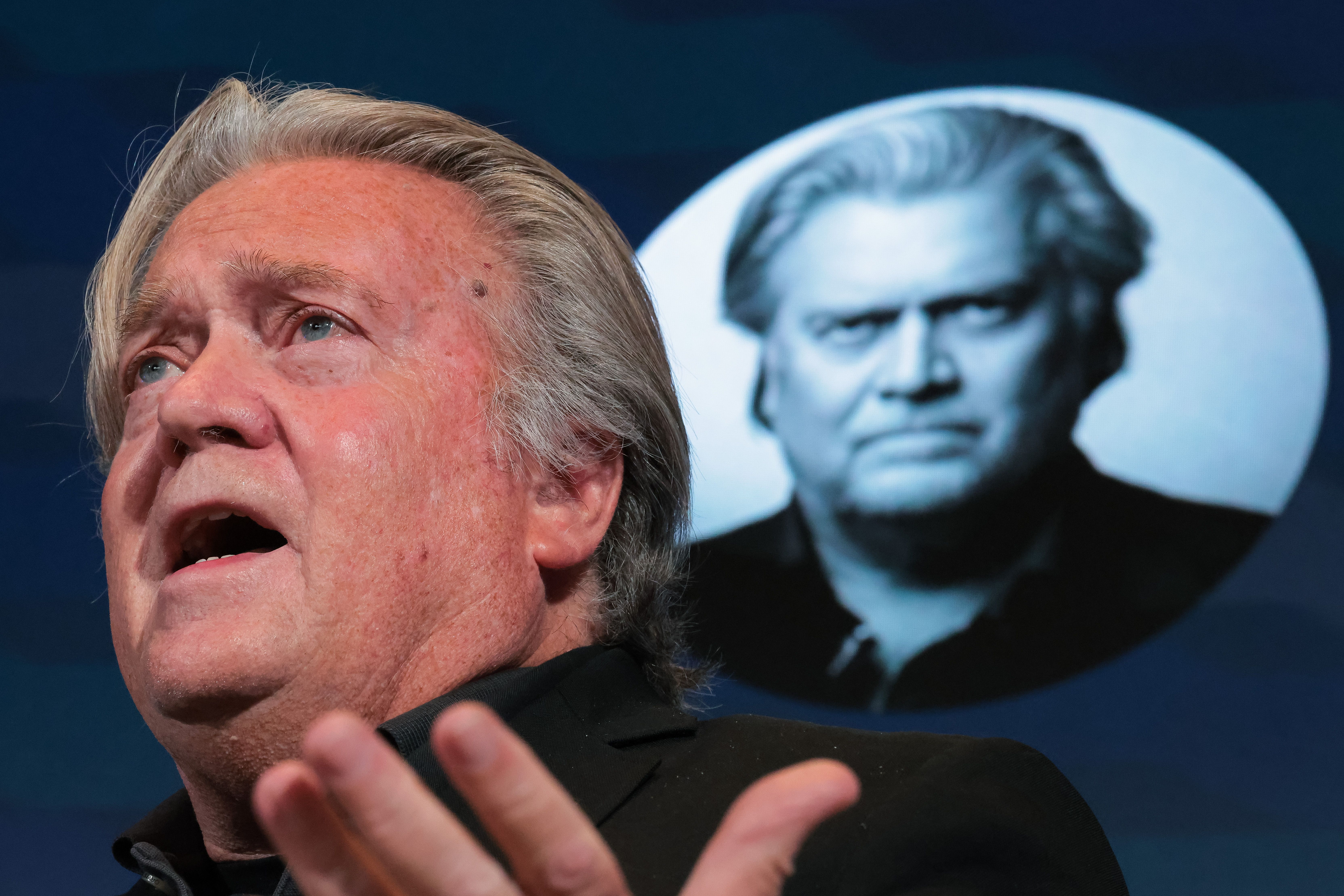 Bannon speaks in front of a screen that's showing a headshot of him