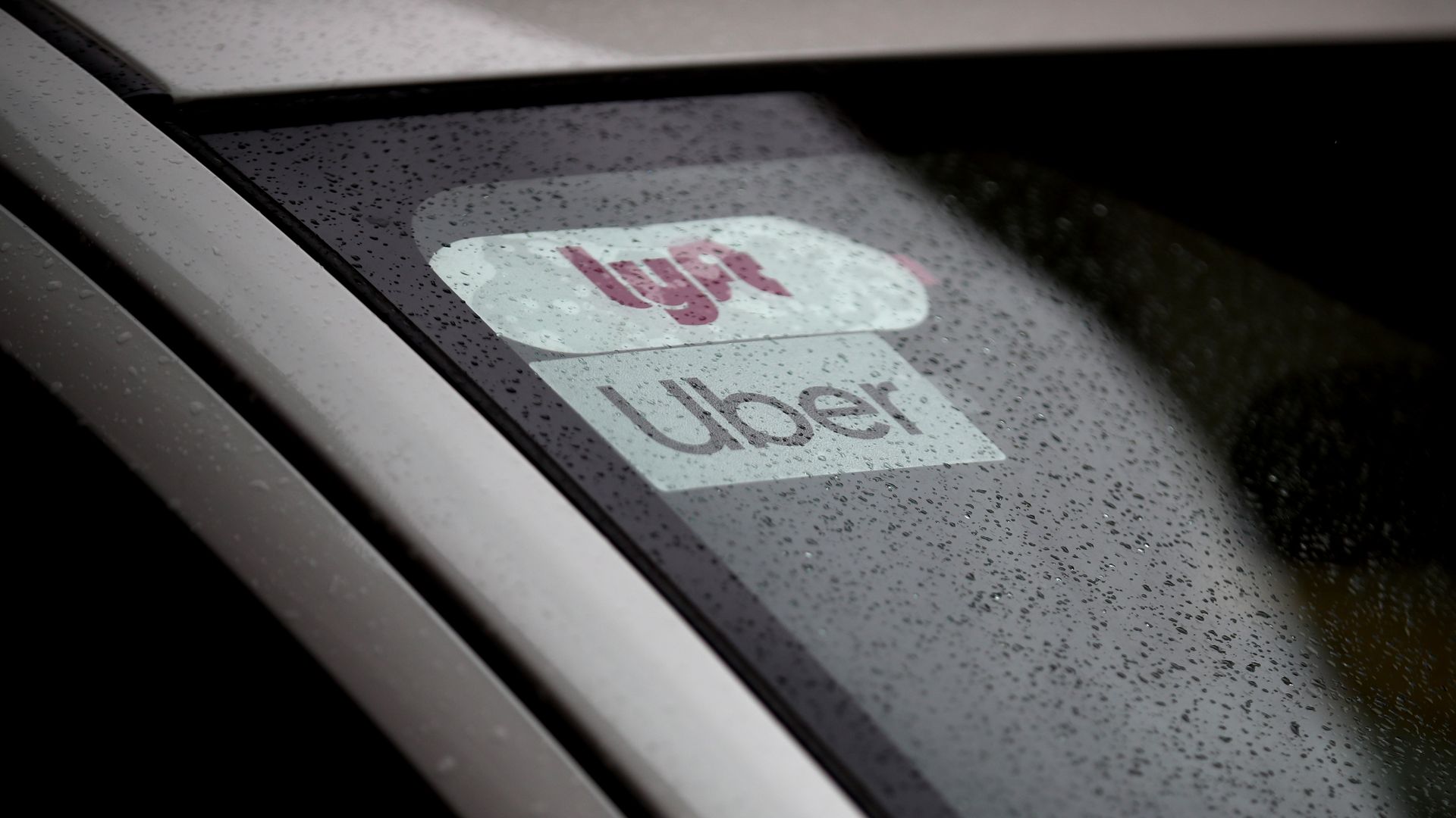 Photo of car with Uber and Lyft logos in the rain. 