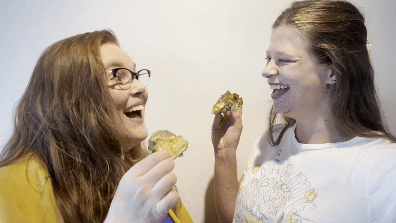 Two women smile at each other as they toast with small slices of king cakes.