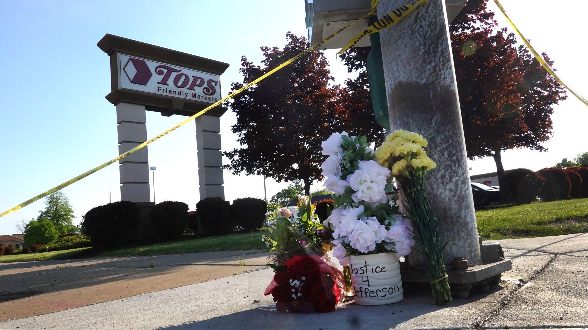 Photo of a flower memorial positioned with the Tops sign standing in the background