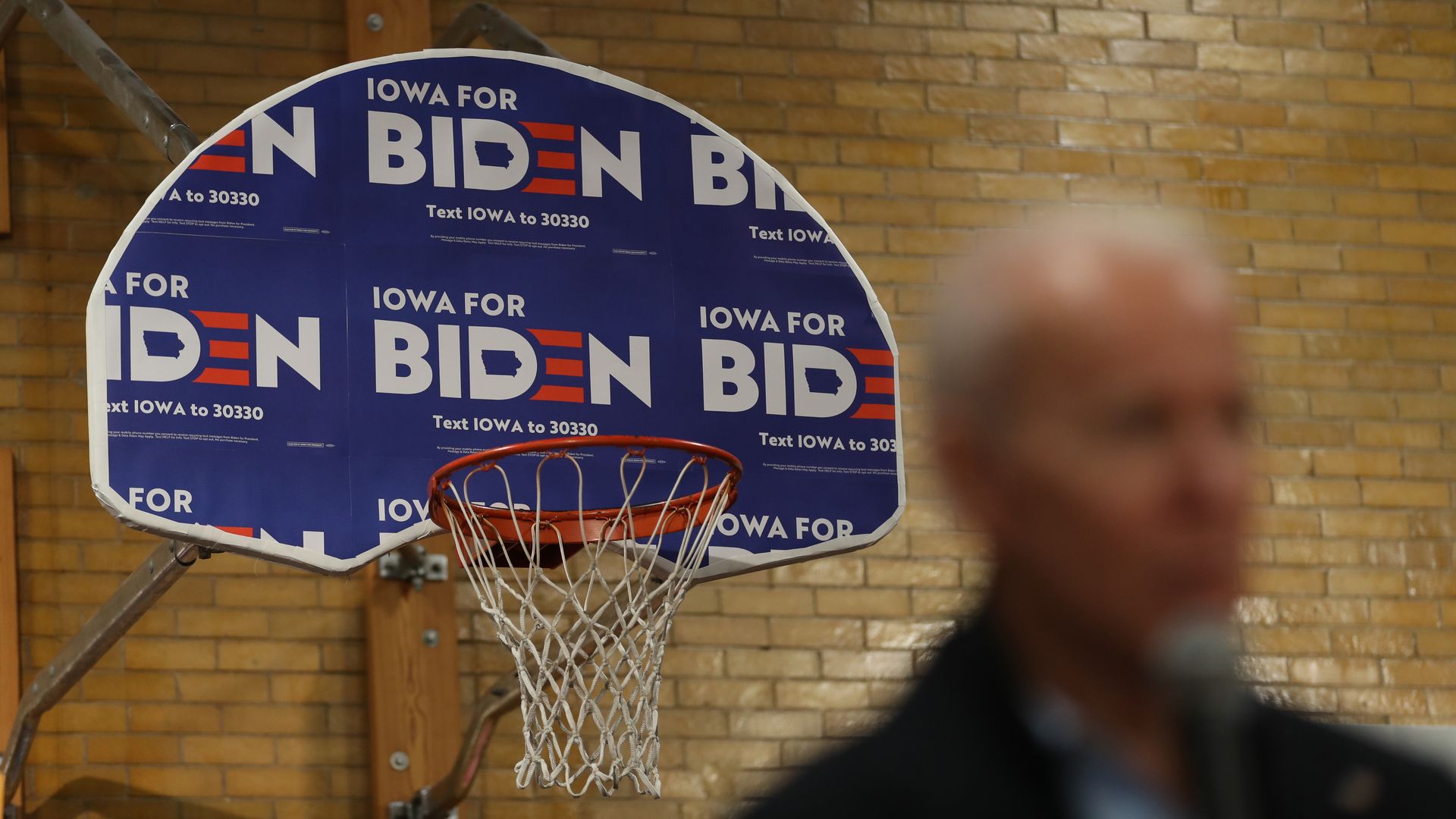 A basketball backboard wrapped in Biden campaign signage is in focus while Joe Biden's face in front of it is blurred