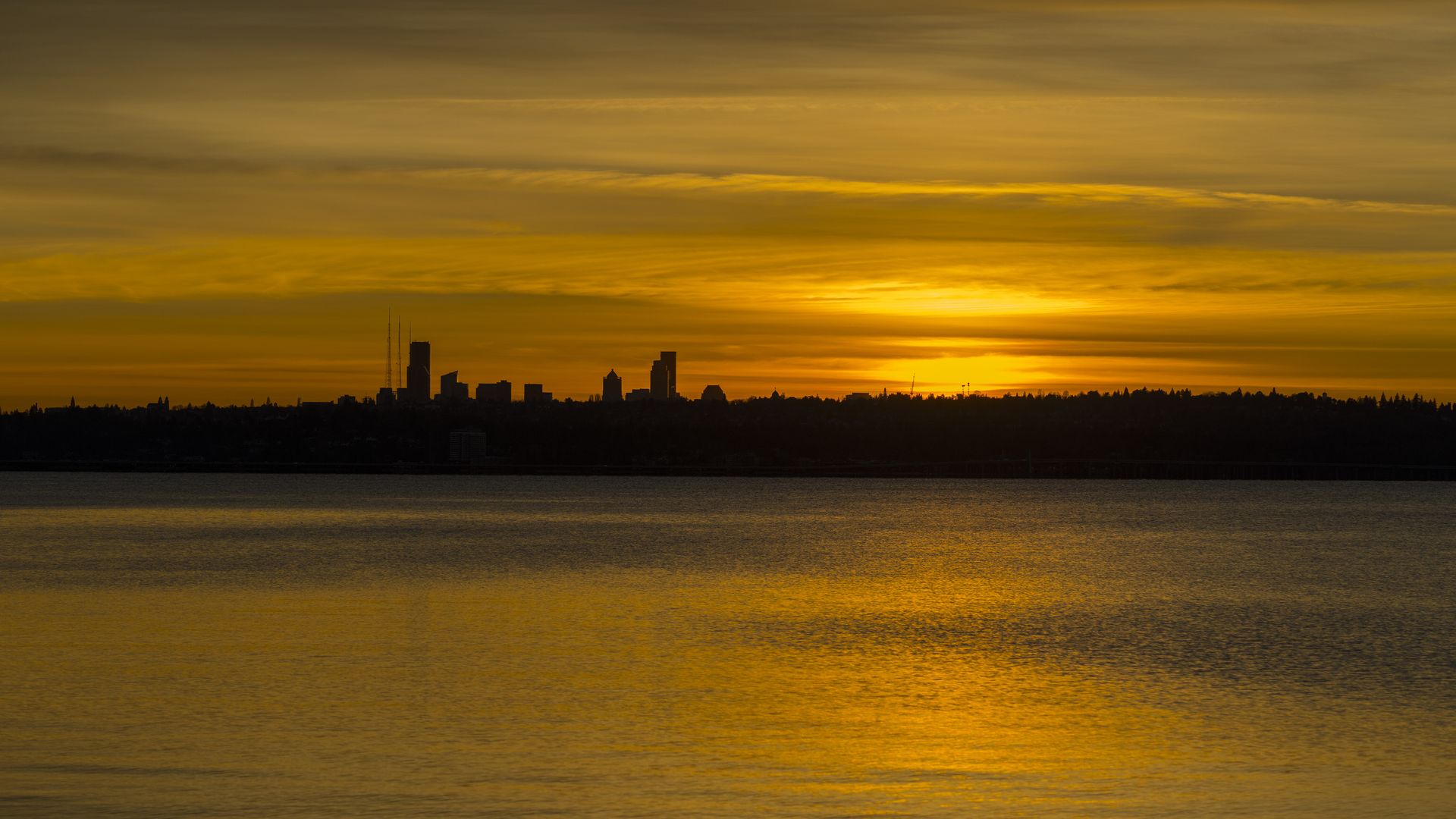 Seattle is silhouetted as the setting sun produces orange skies and orange reflections on Lake Washington.
