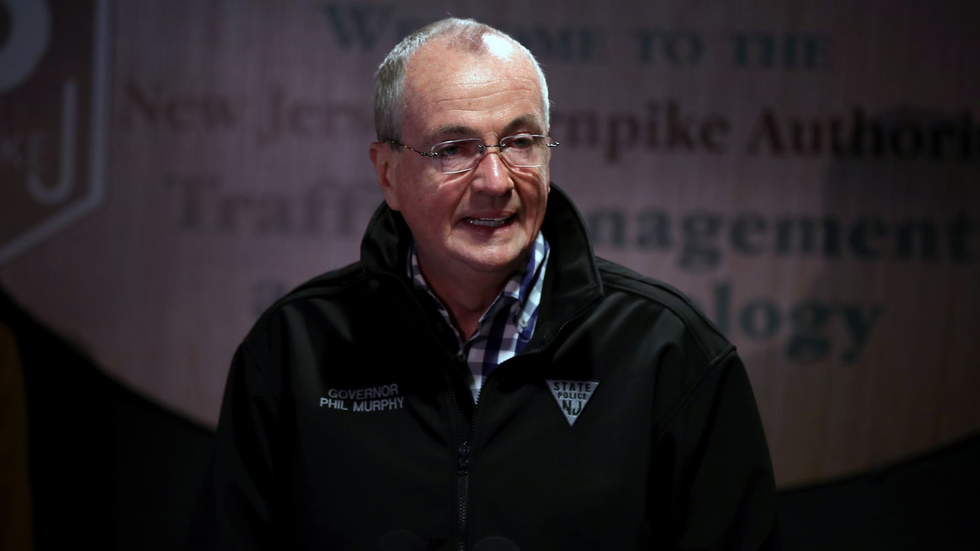 New Jersey Gov stands in a plaid shirt and windbreaker 