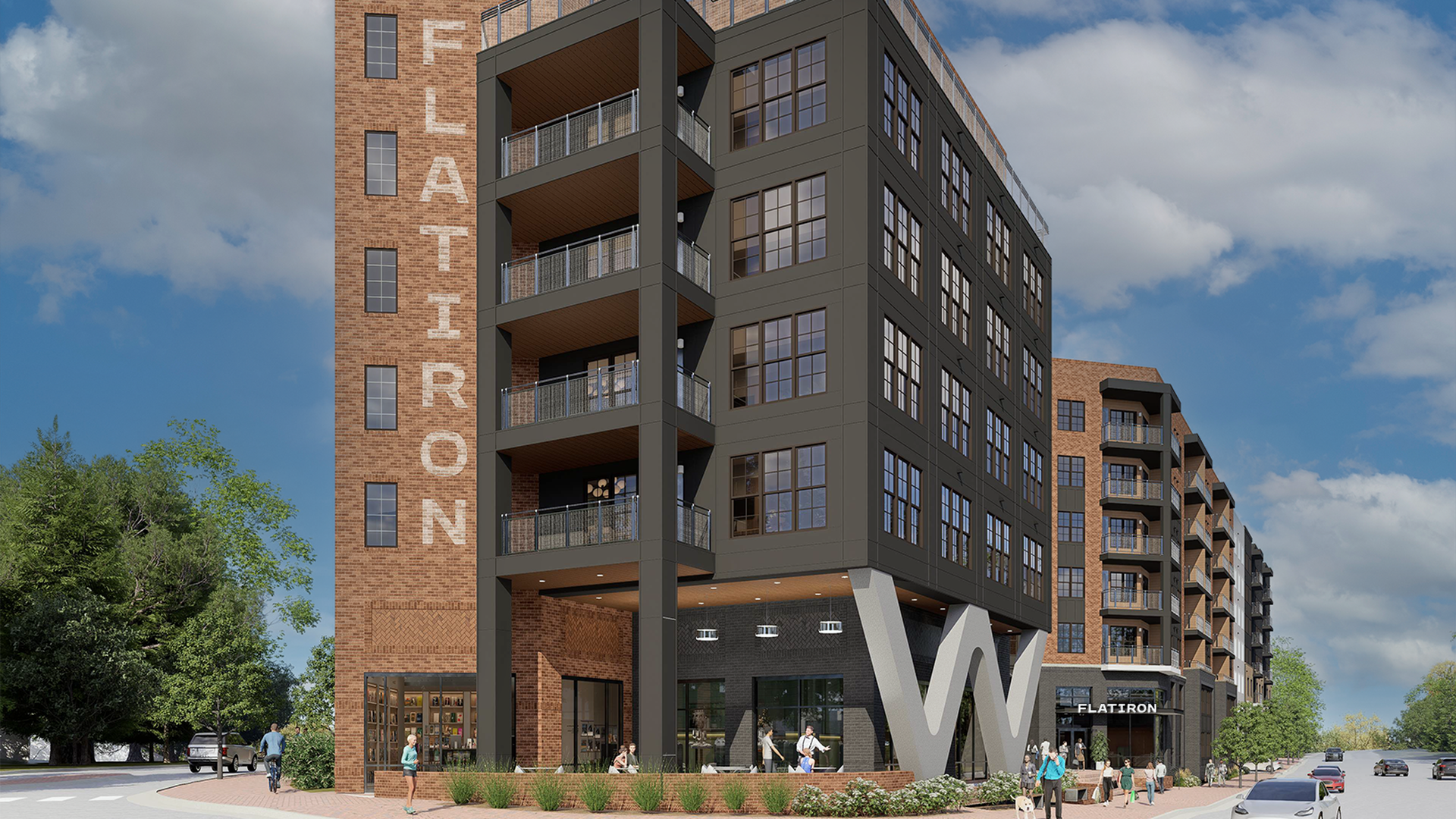 Modern mixed-use building: a brick tower with vertical "FLATIRON" on the left, and a dark gray multi-story facade with balconies and large windows; people walk in a plaza under a blue sky.