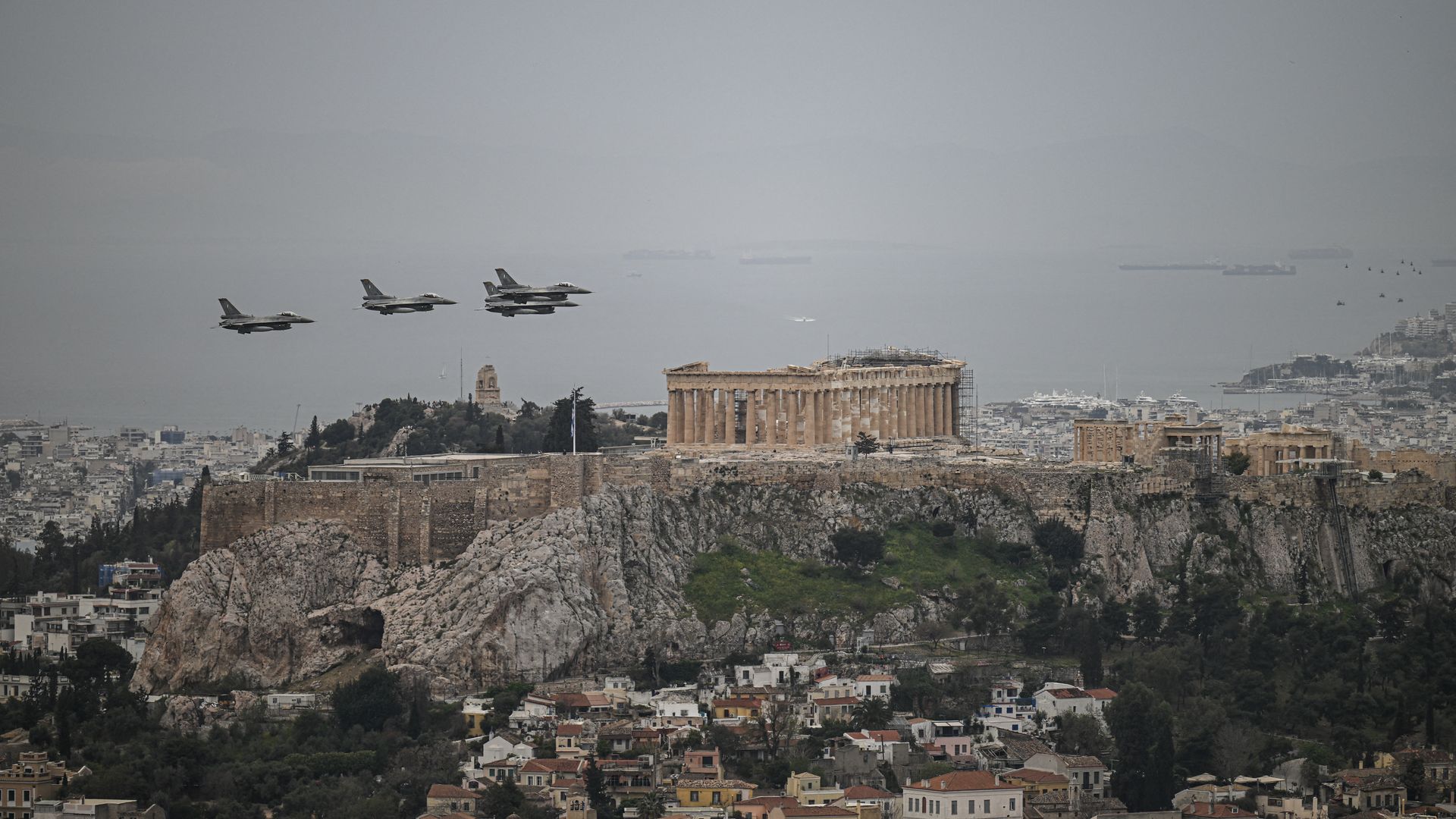F-16s fly over the Parthenon and Acropolis. The city and water can be seen from afar.