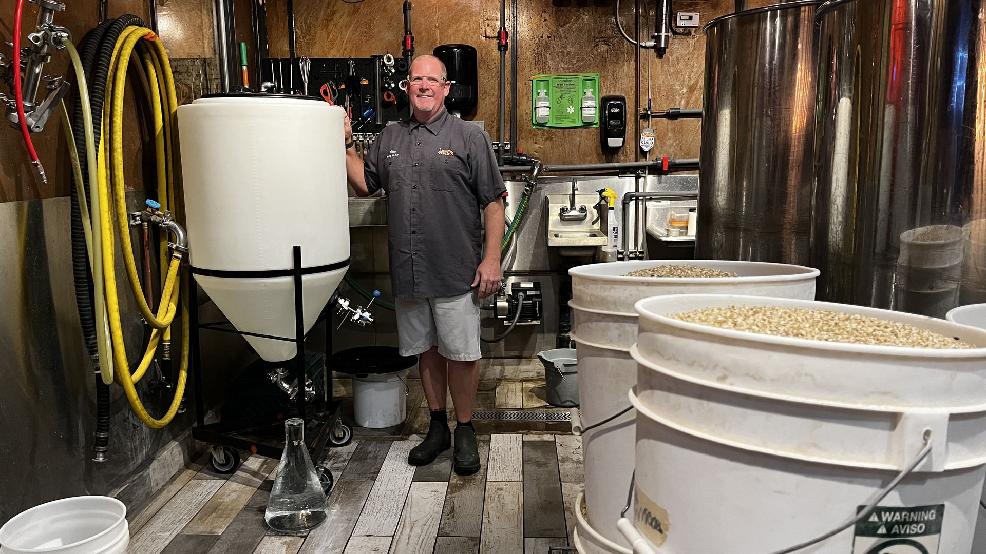 A man smiling next to a large water tank with buckets of wheat in the foreground.