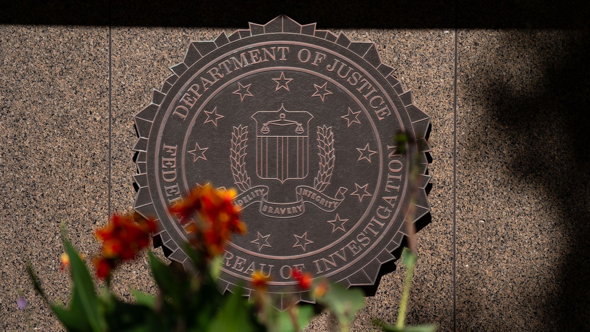The DOJ FBI logo is seen behind flowers, which are blurry