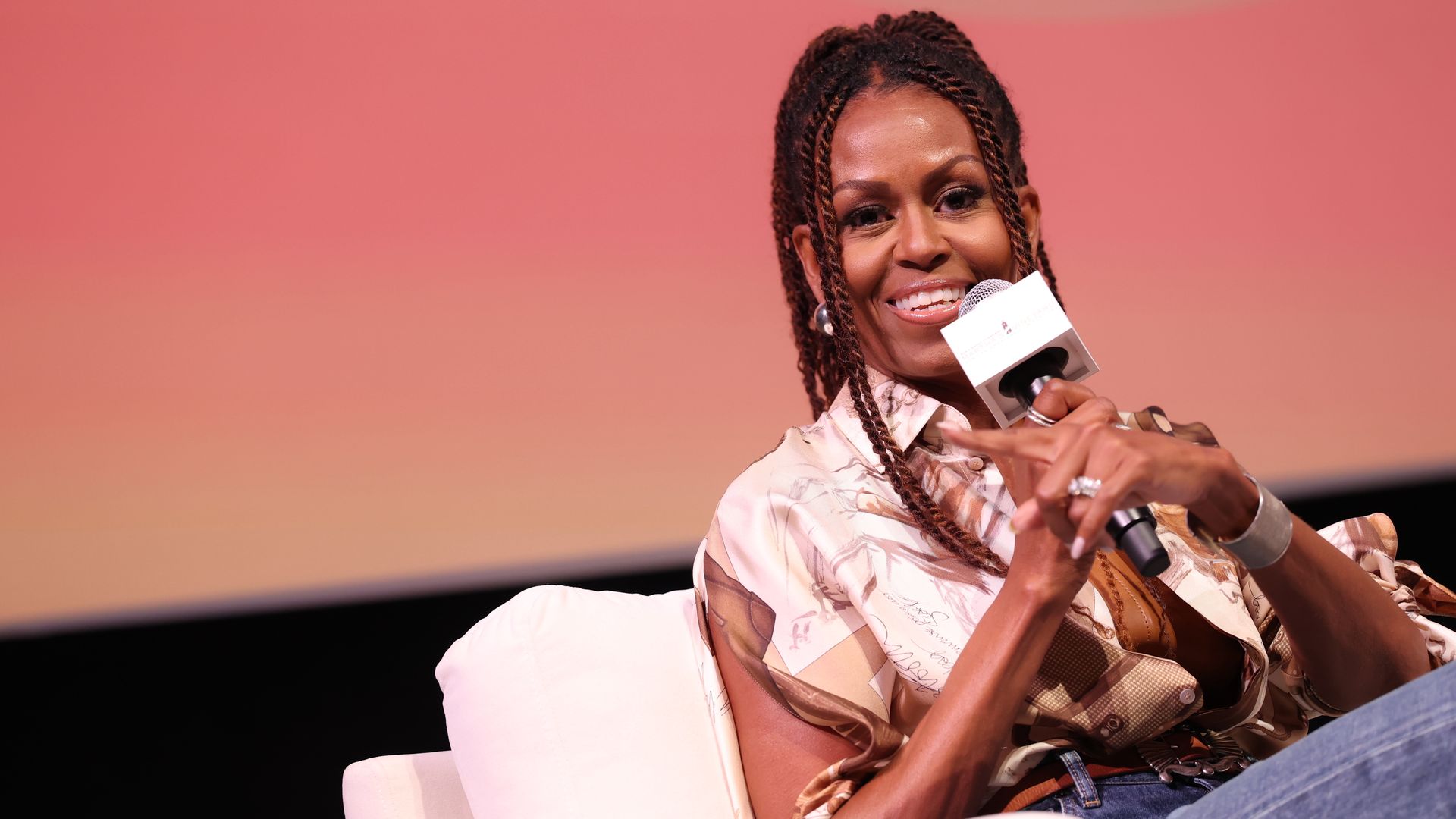 Image shows Michelle Obama talking into a microphone.