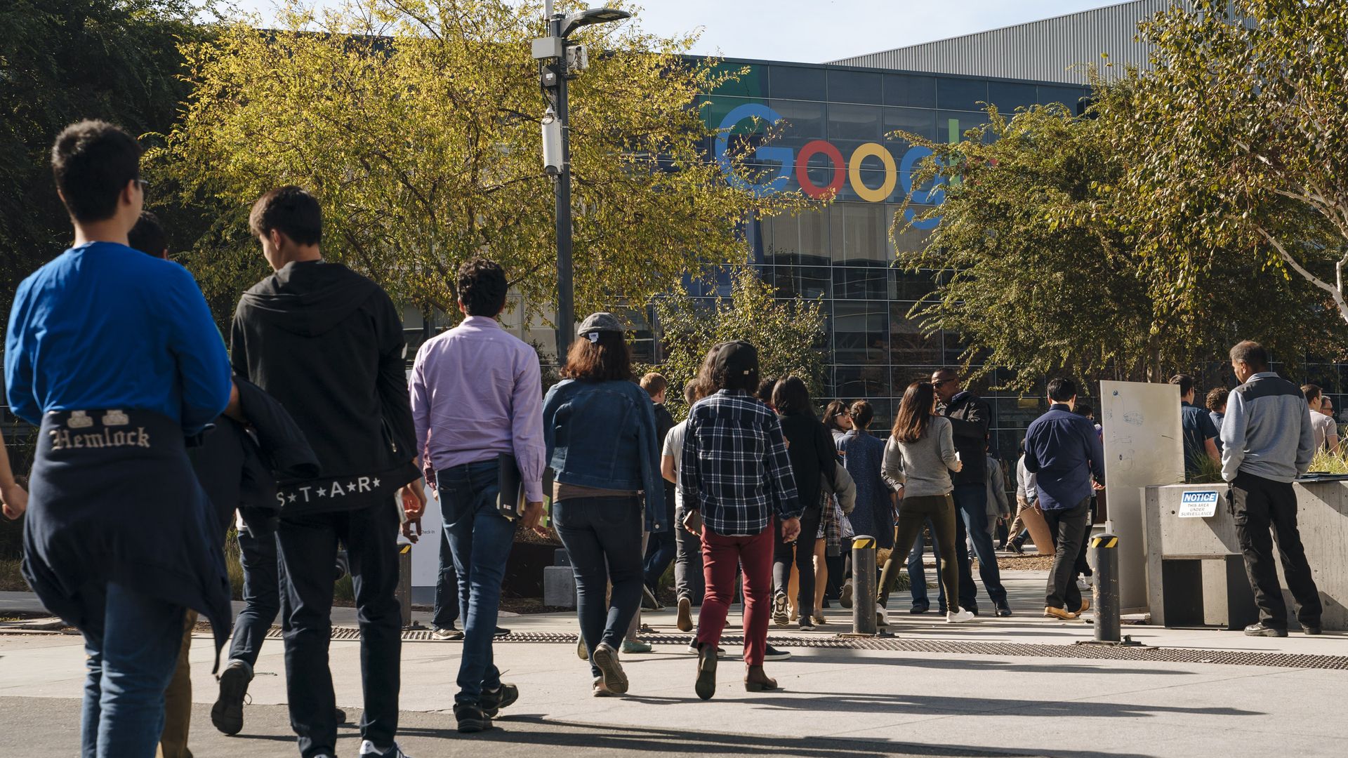 Google employees walkout in diagonal line with Google logo in background.