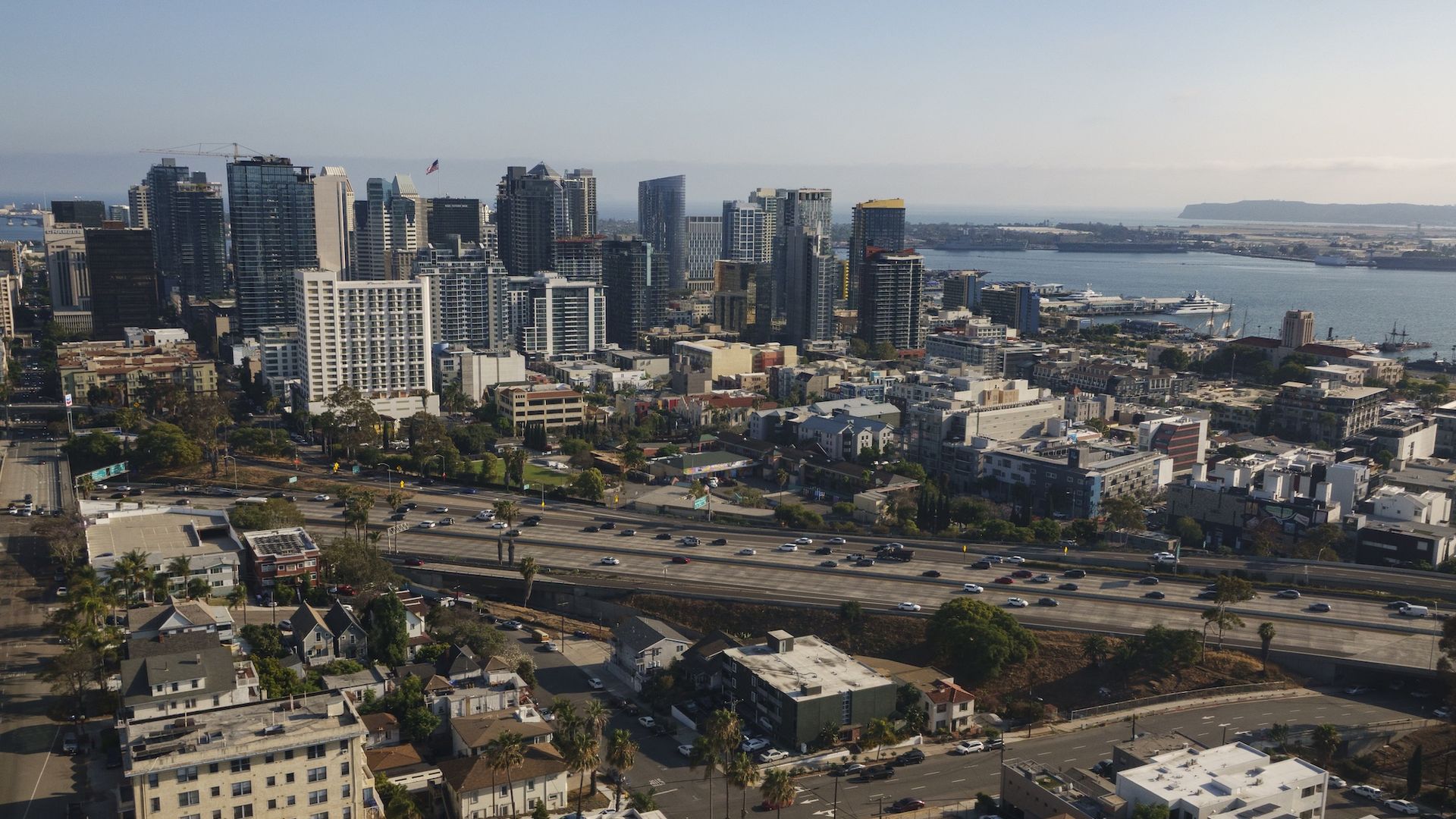 Aerial view of downtown San Diego, showing high-rise buildings along the waterfront, a busy freeway, and residential neighborhoods with smaller buildings.