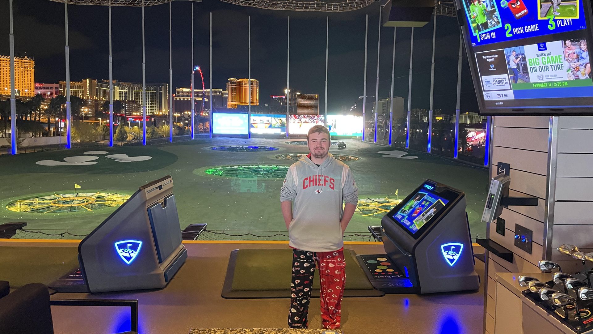 A young person at a top golf with the Vegas skyline in the background. 