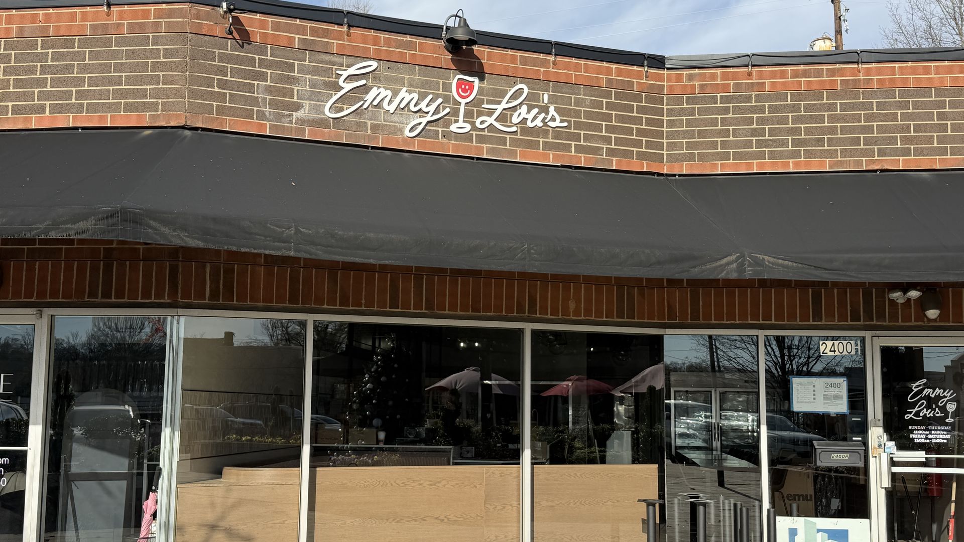 Exterior of Emmy Lou's restaurant with red and brown brick facade, black awning, and glass windows reflecting parked cars and sky.