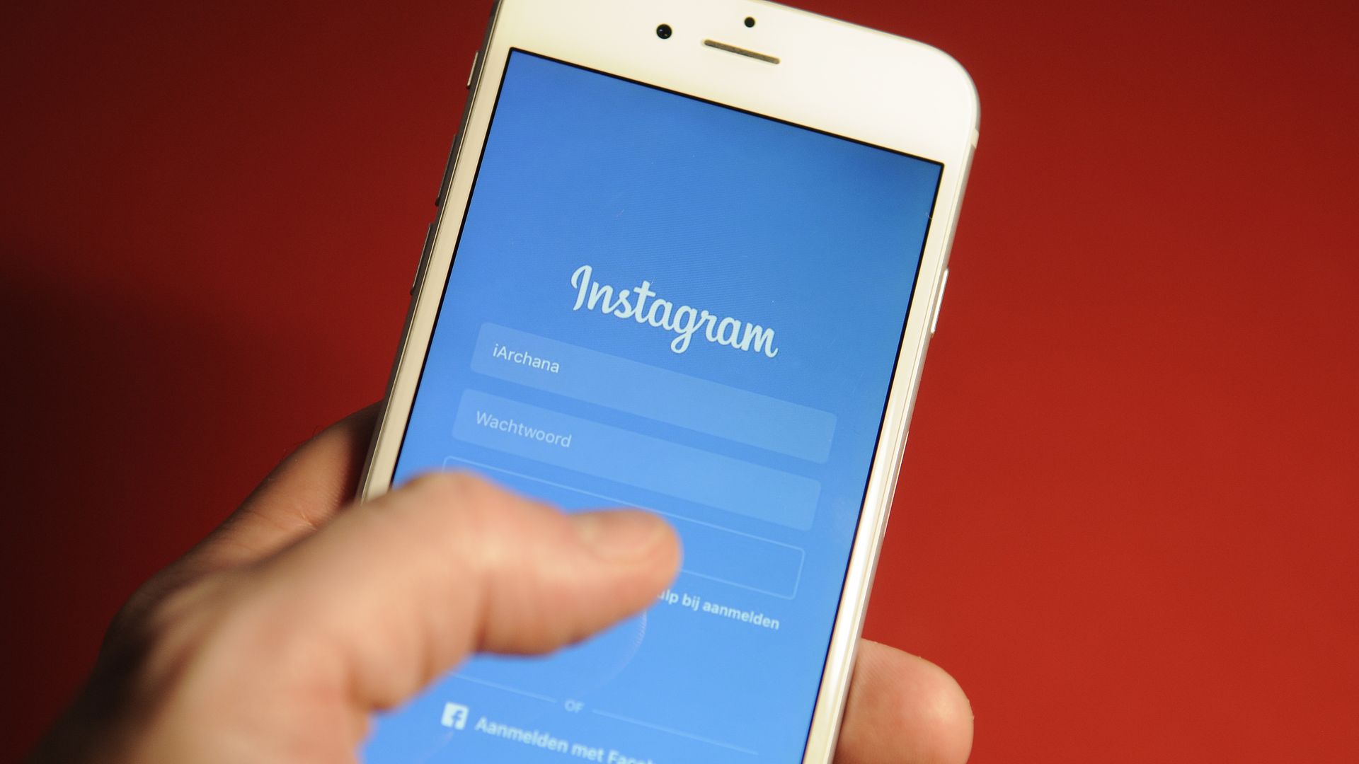 Hand holds phone on Instagram login page over red background