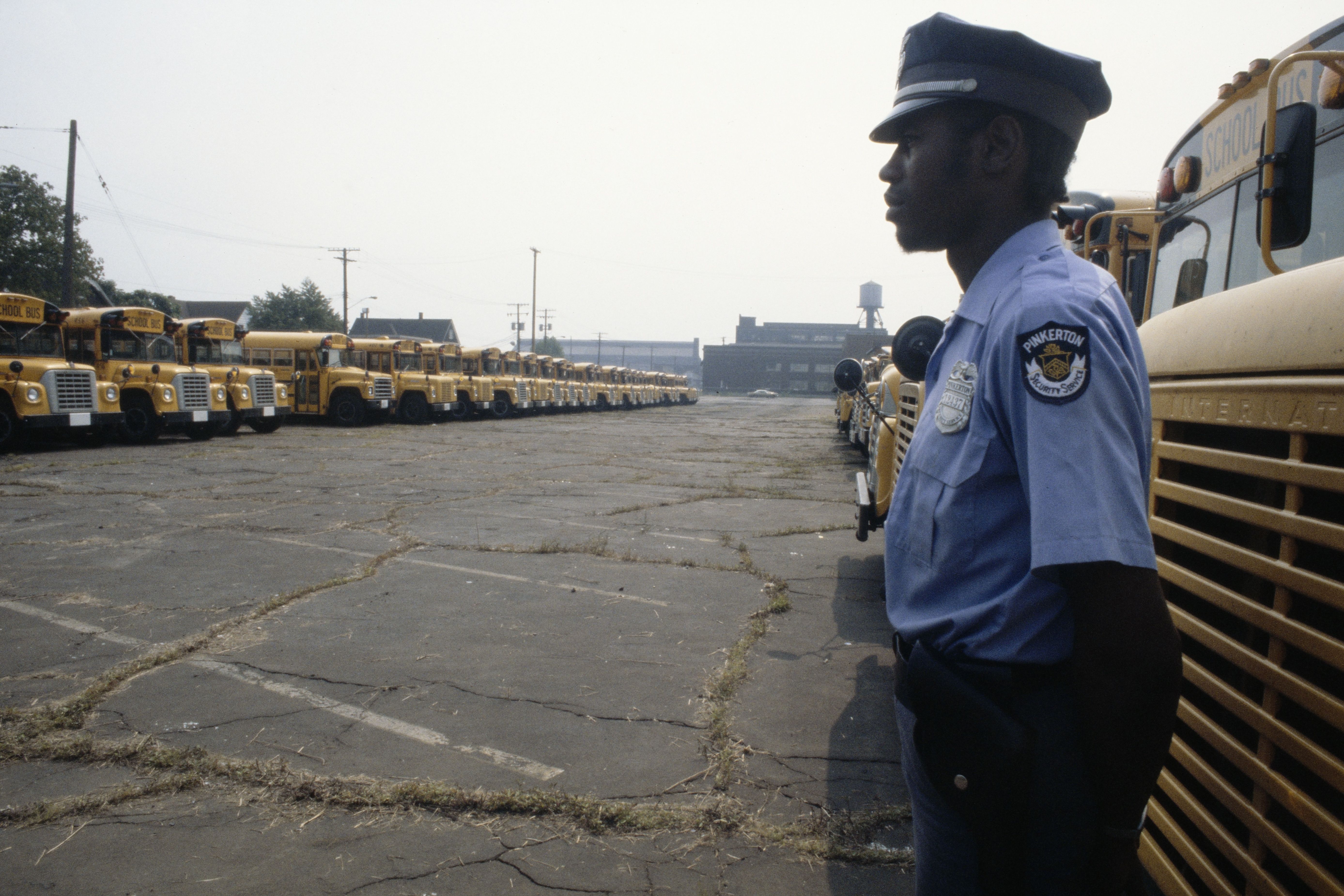 A black security guard standing in a bus lot