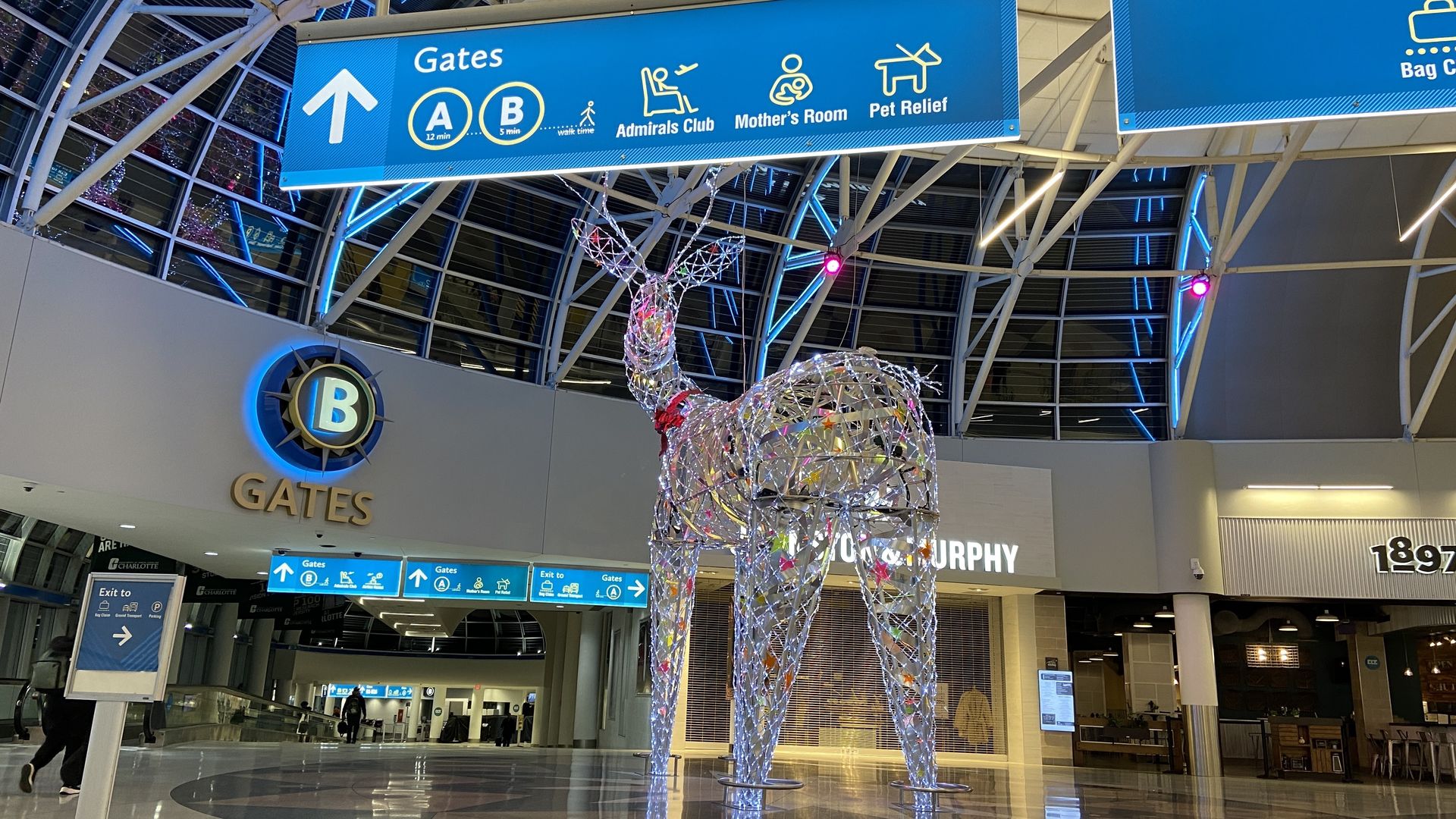 Massive lit up reindeer in the Charlotte Douglas International Airport atrium in front of a sign pointing toward B gates. 
