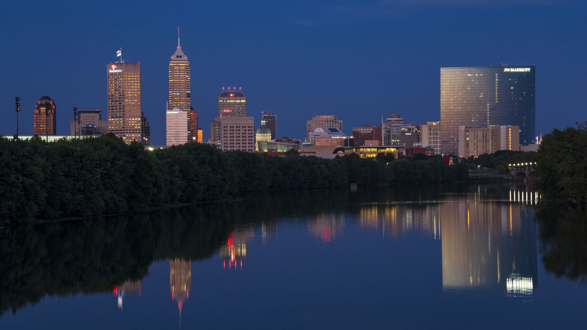 Skyline view at sunset into dusk of Indianapolis buildings on White River reflect in water.
