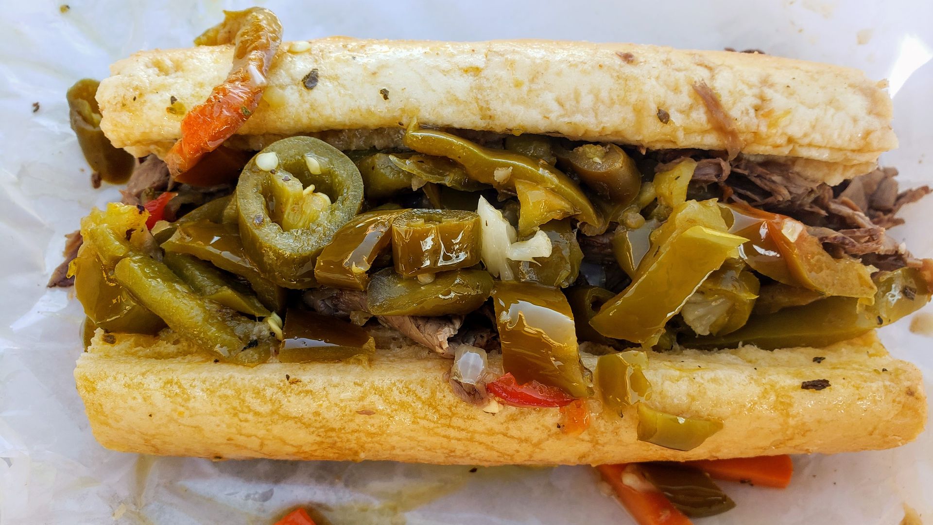 Toasted sub stuffed with shredded meat and a heap of green pickled peppers, onions, and a few red peppers, all overflowing from a thick crusty roll.