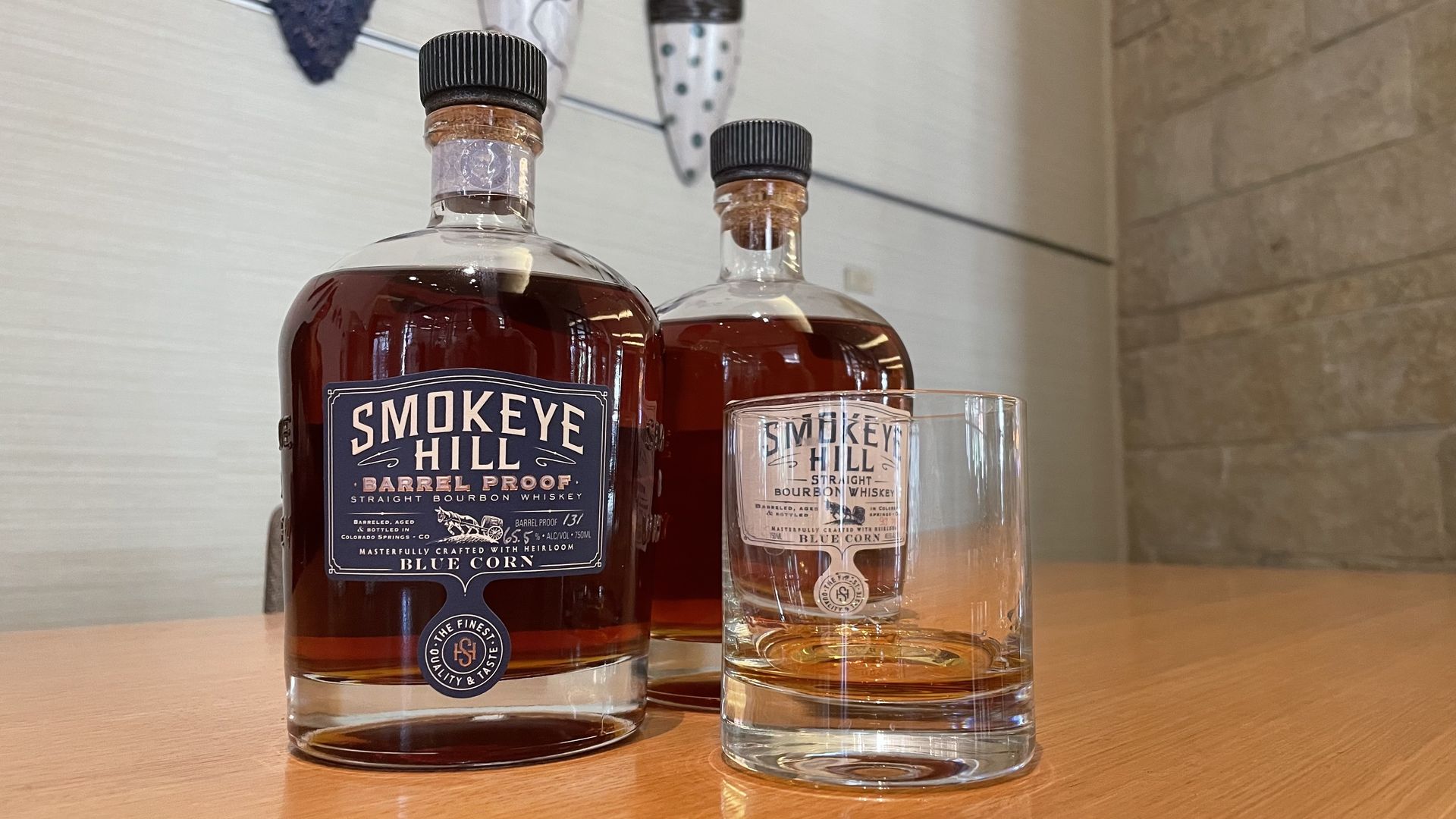 Two bottles of brown whiskey are places near a clear whiskey glass. 