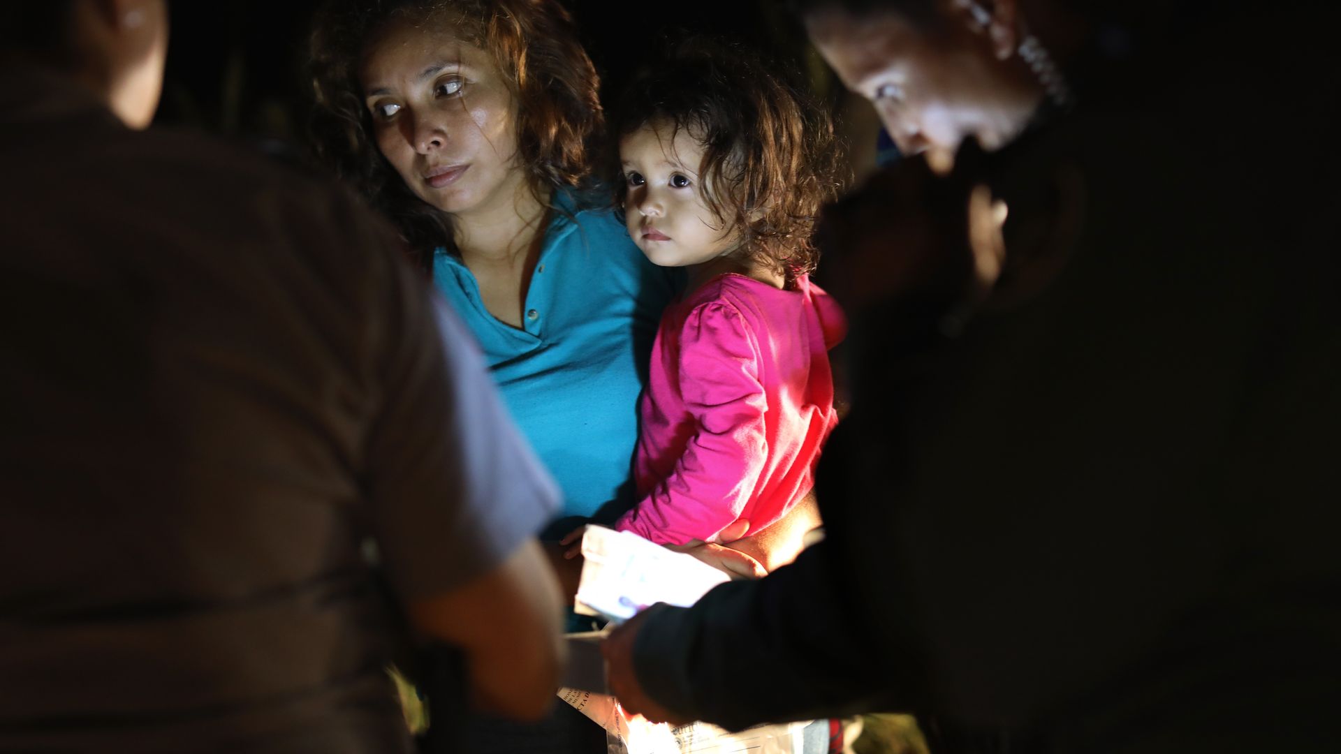 An immigrant holds her daughter while having paperwork looked at by immigration law enforcement officials