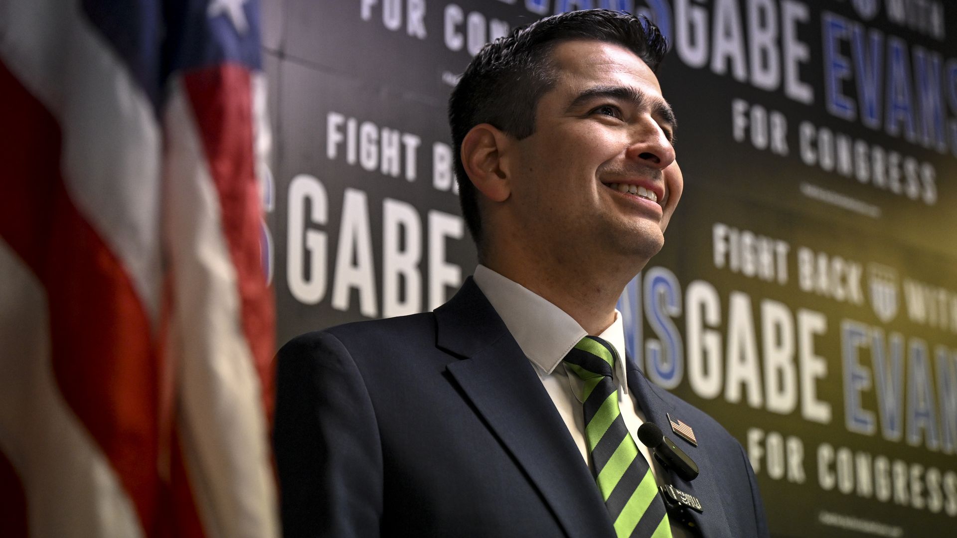 A man in a suit and green tie smiles.