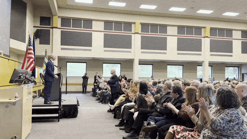 Animate GIF shows a man, Portland Mayor Keith Wilson, in front of a crowd as they rise to give him a standing ovation.