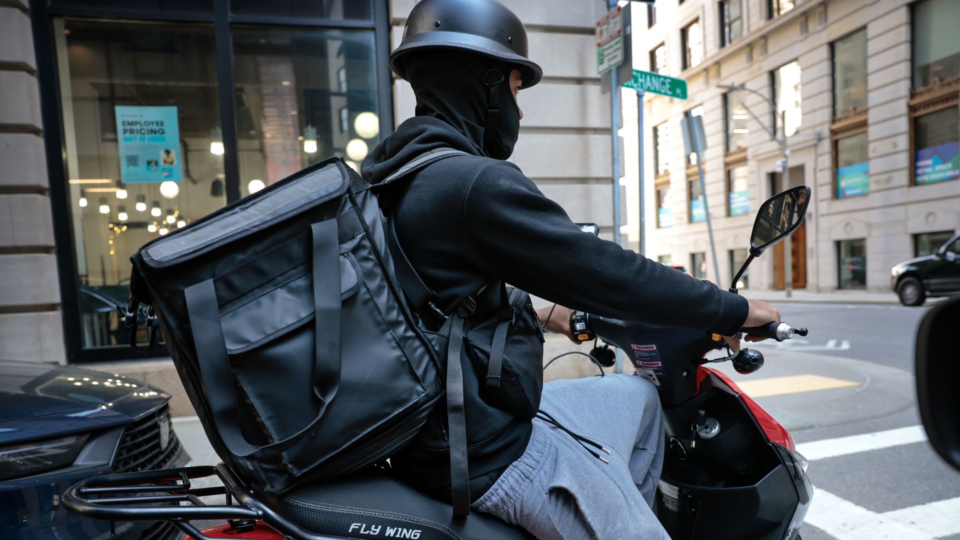 A delivery driver with a bag for food on a motorized scooter waits at a stop sign.
