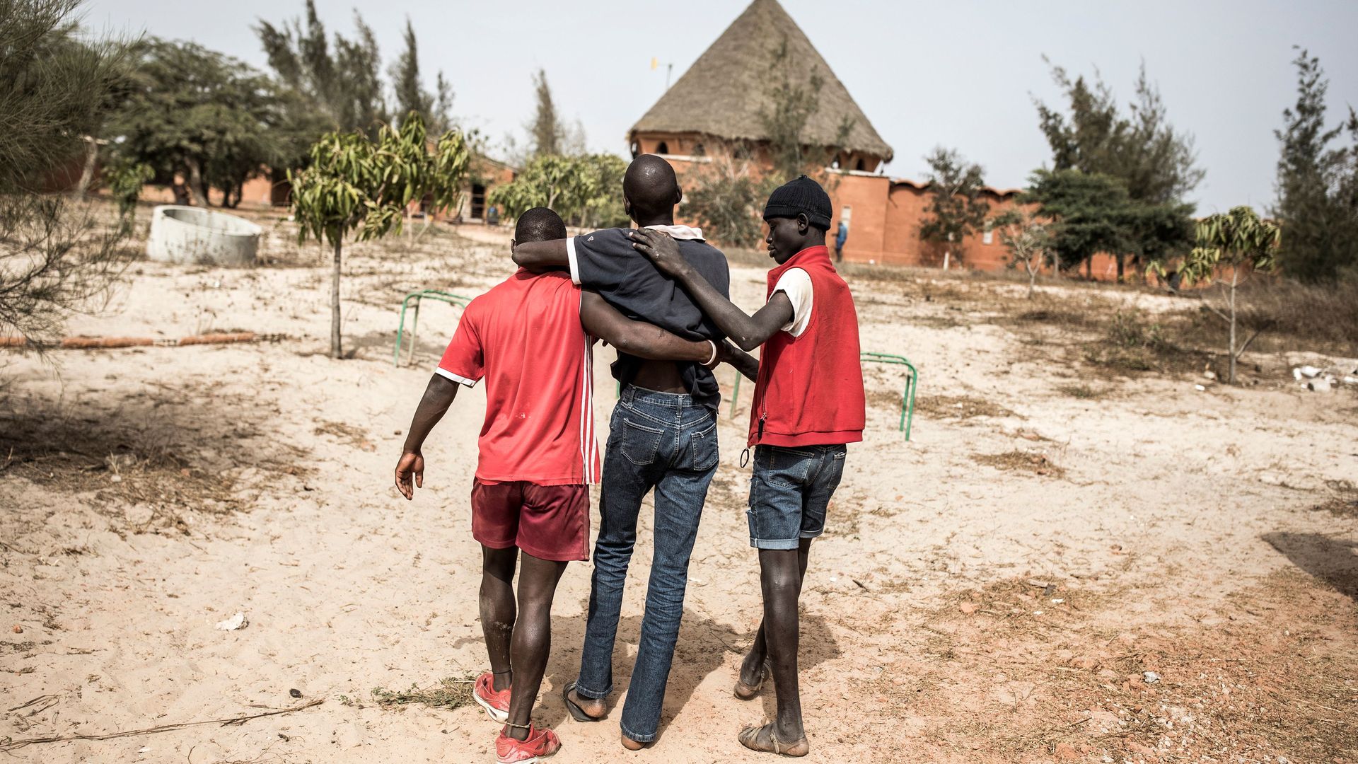 In this image, two boys help a boy walk