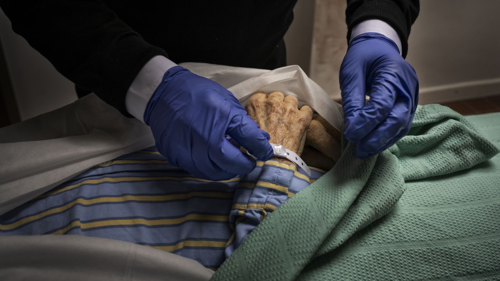 An employee of Taunton Funeral Services attaches a name tag to the wrist of a patient who died that morning of suspected COVID-19 in a nursing home.