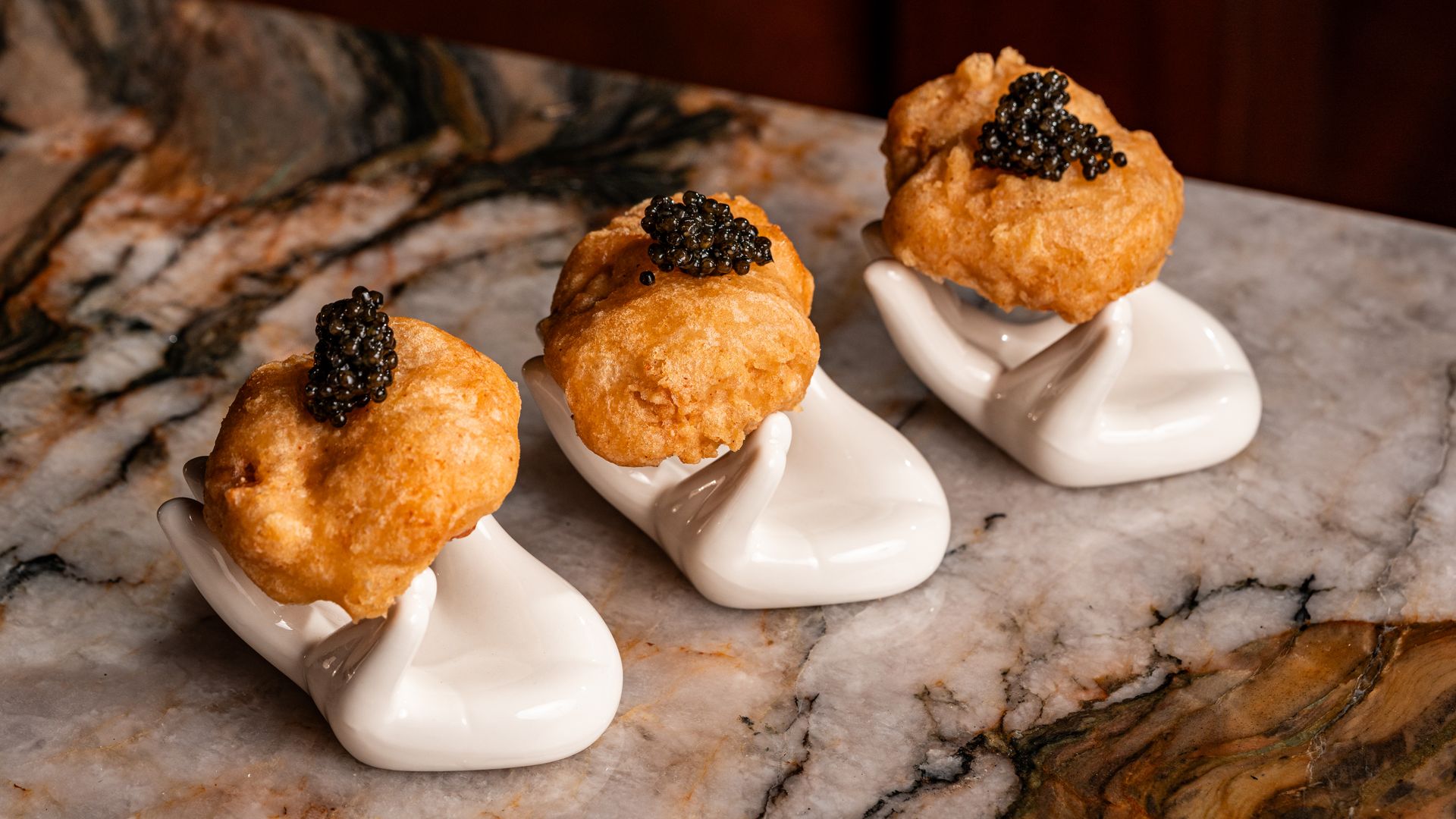 Caviar-topped chicken nuggets on miniature hand-shaped plates on a marble counter top