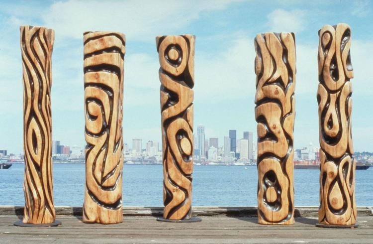 Carved cedar poles with blacked designs overlook the Seattle waterfront. 