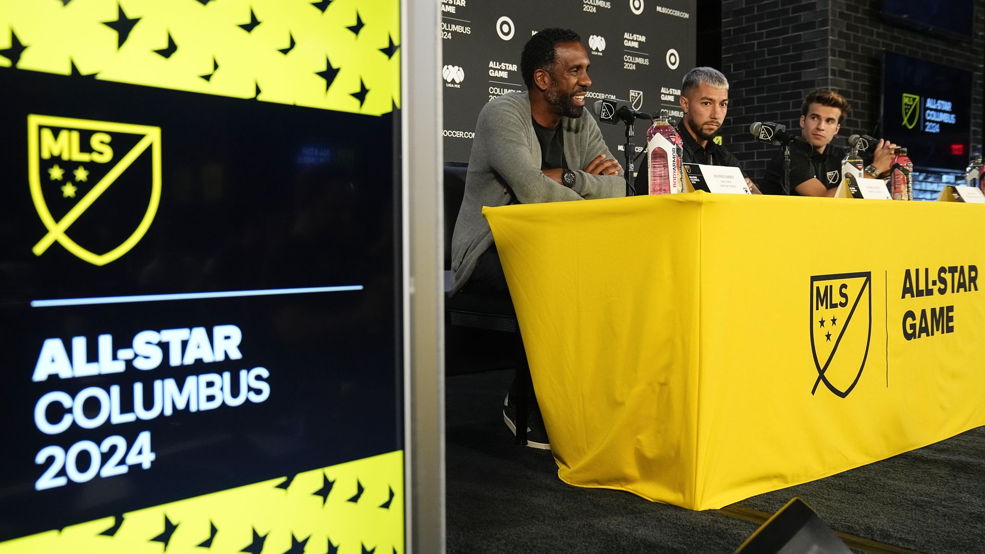 Crew head coach and MLS All-Stars head coach Wilfried Nancy sits at a press conference in the background, with an "All-Star Columbus 2024" sign in the foreground