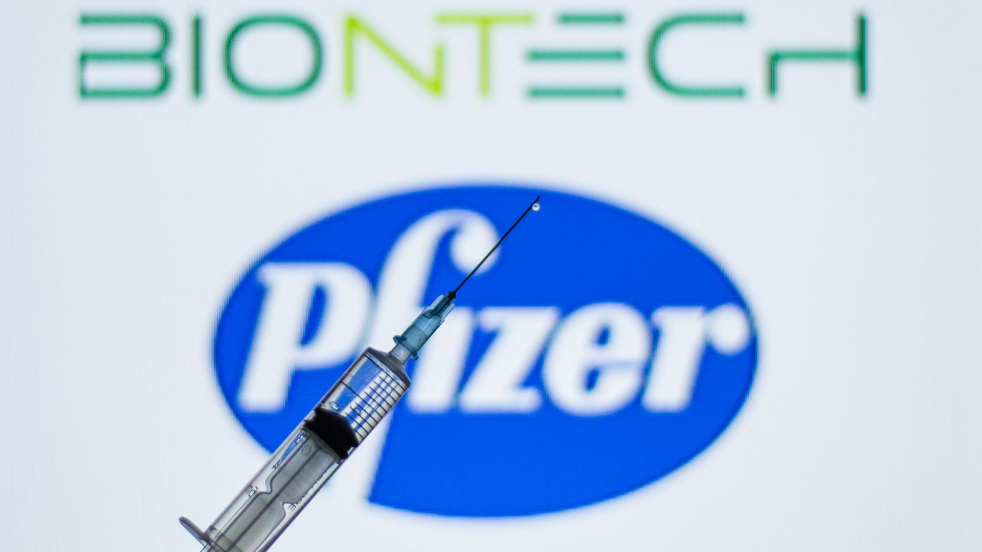 a syringe seen in front of the Pfizer and BioNTech logo