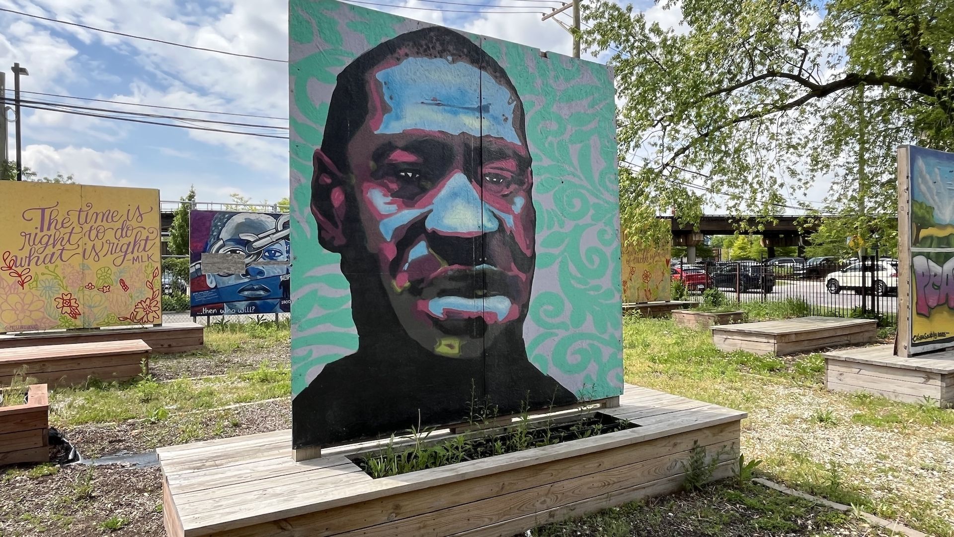 A mural with George Floyd's face on a wood board in a garden.