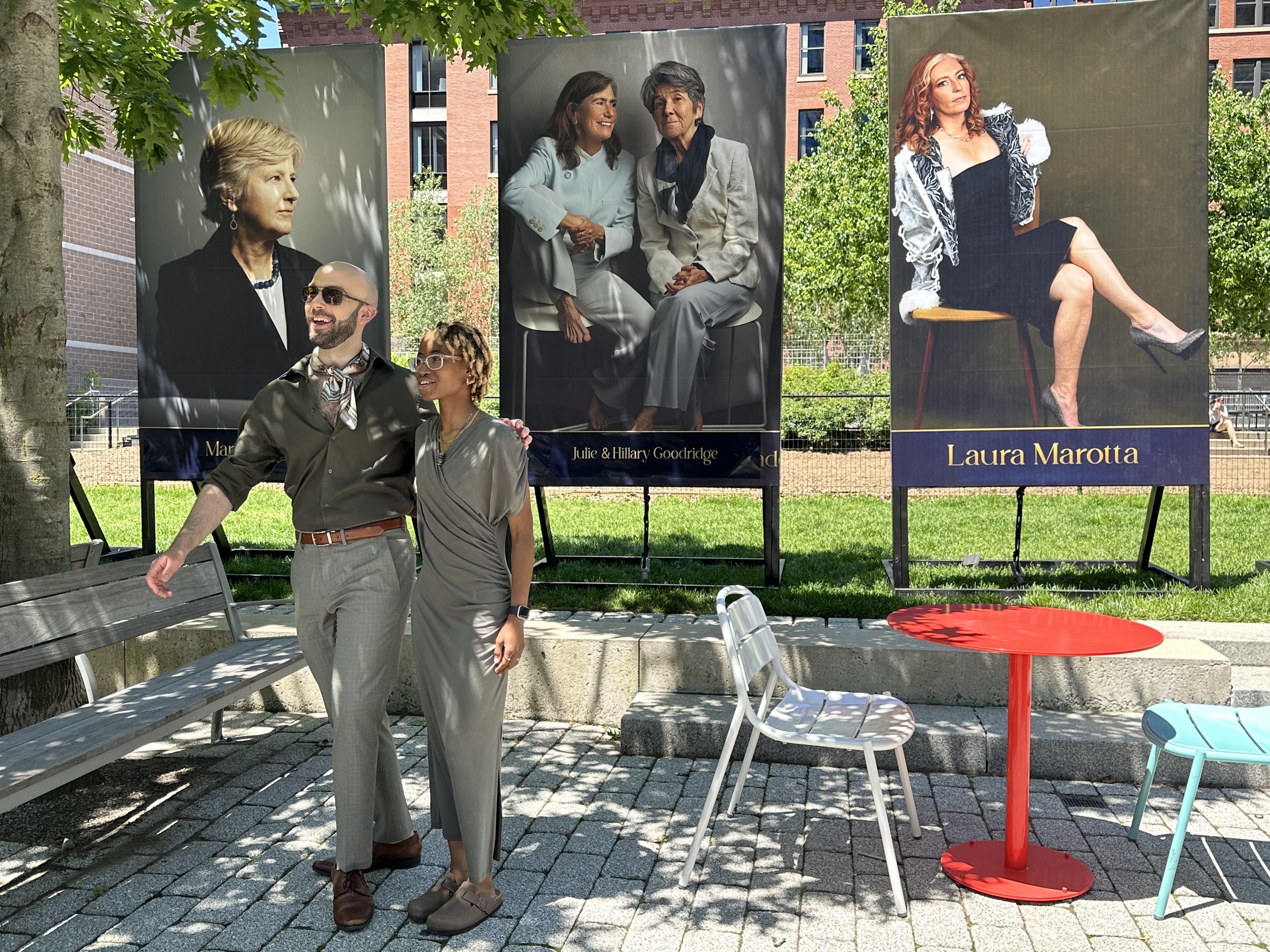 Ben Flythe and Marcia Williams, two photographers of the Portraits of Pride project, pose for a photo in front of their portraits in the Seaport Sea Green.