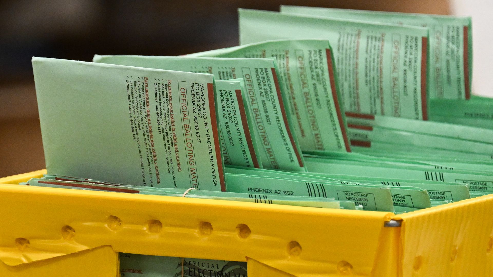 Green official ballot envelopes from Maricopa County Recorder's Office in a yellow plastic bin, ready for processing or counting.