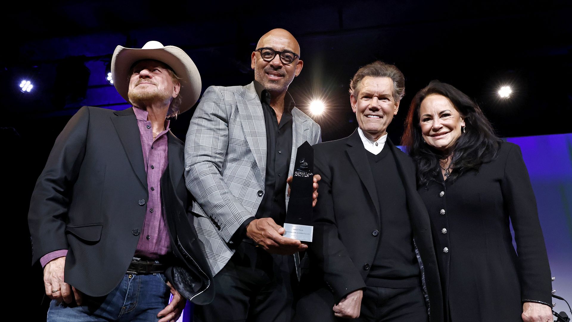Four people stand in a line with one holding an award
