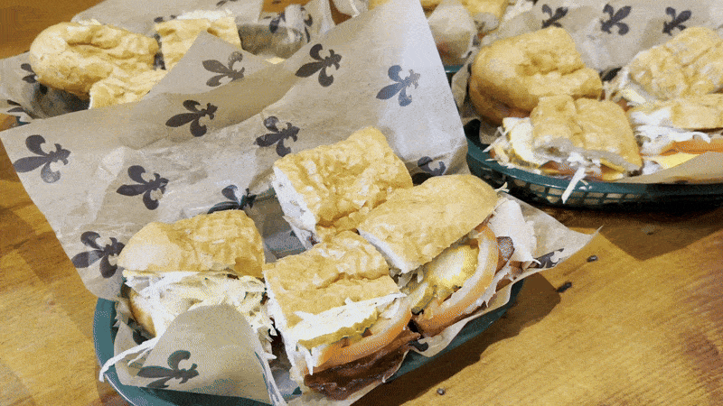 A camera pans over a wooden tabletop filled with poboys.