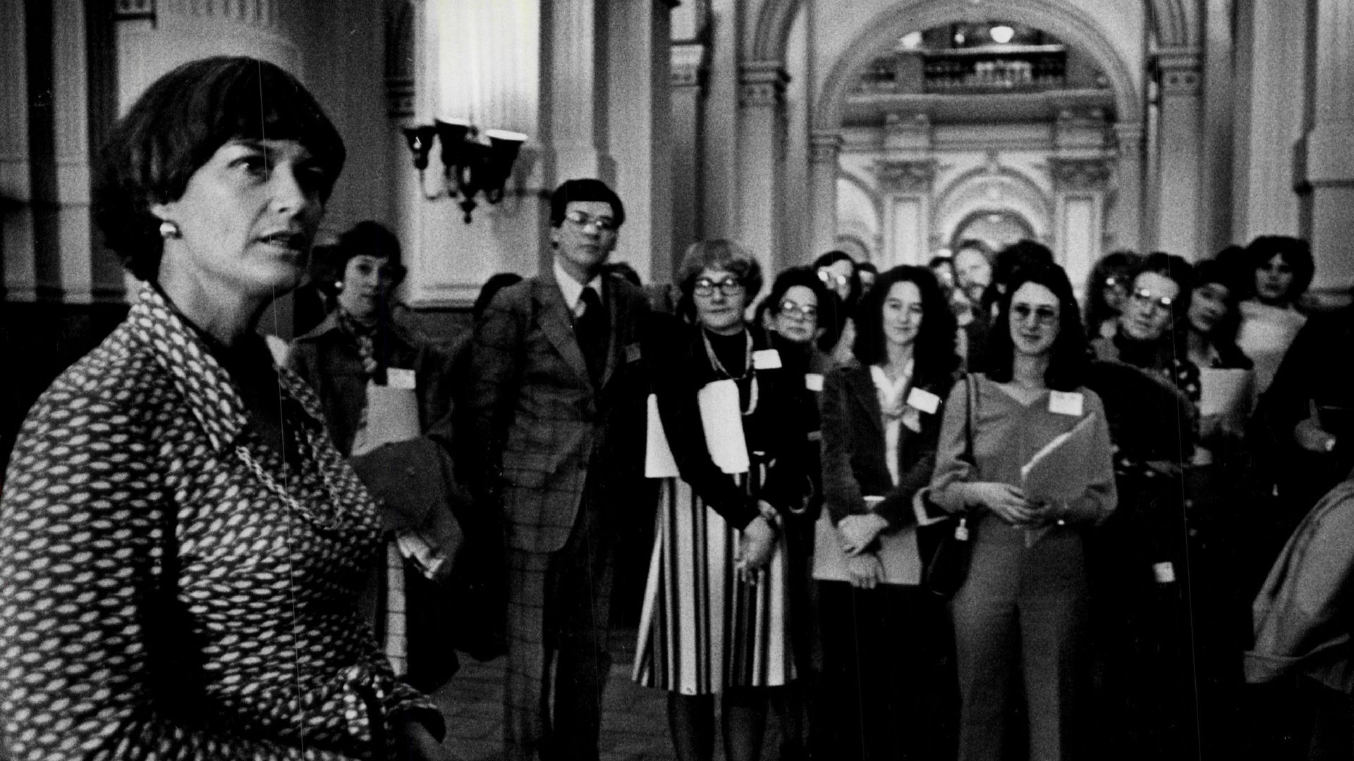 A woman in the foreground looks on as several women in the background look toward her.