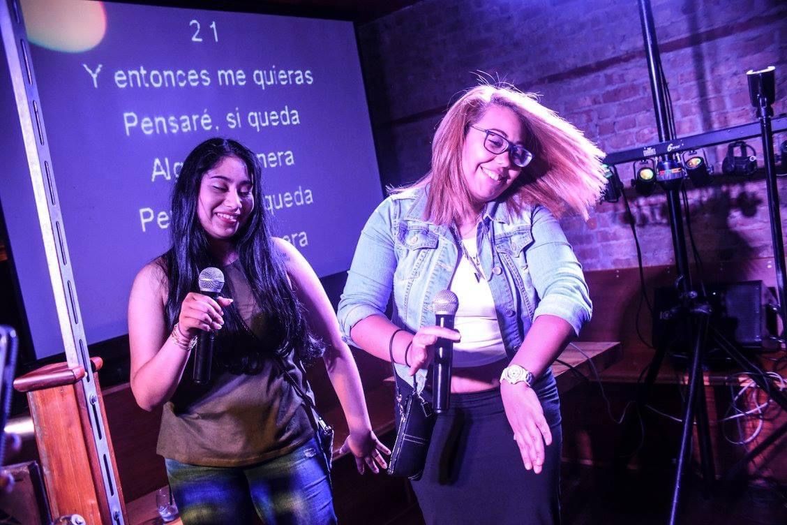 Photo of people using microphones to sing on stage at a bar.