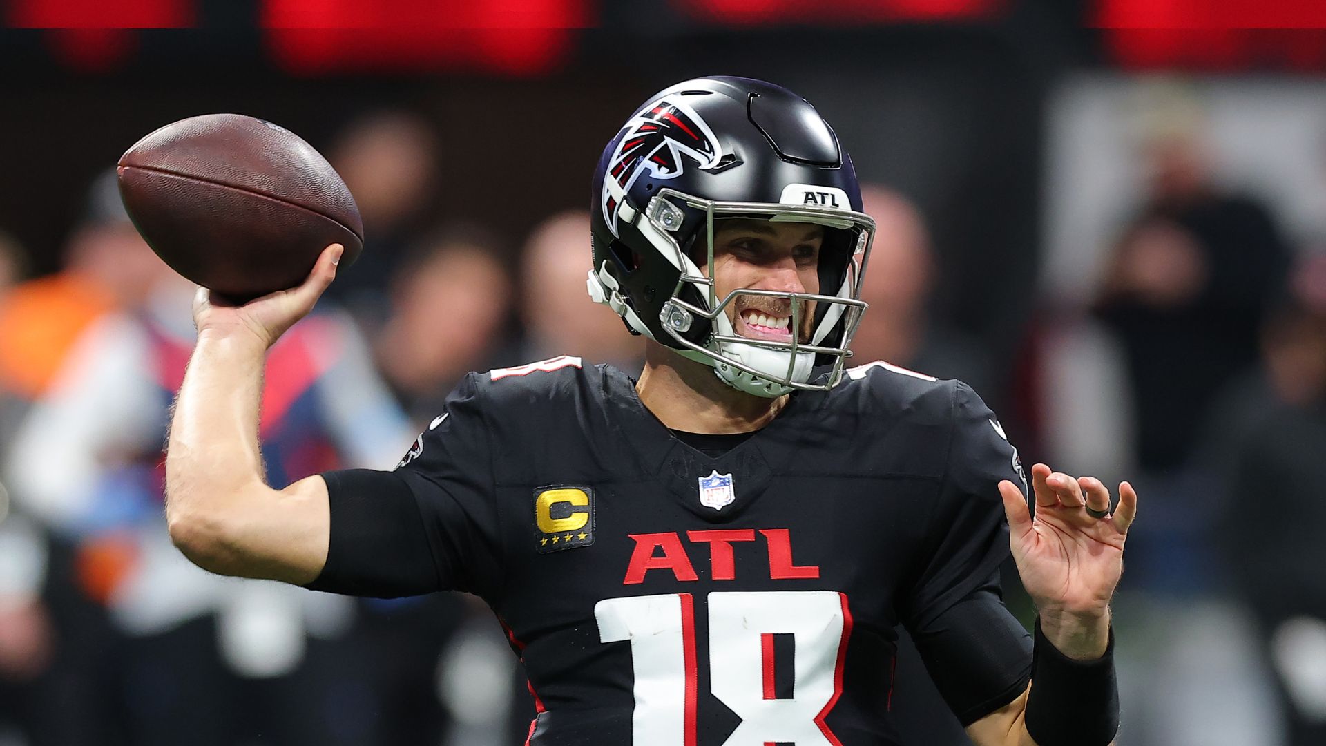 A man in a black football uniform grimaces as he's throwing the ball