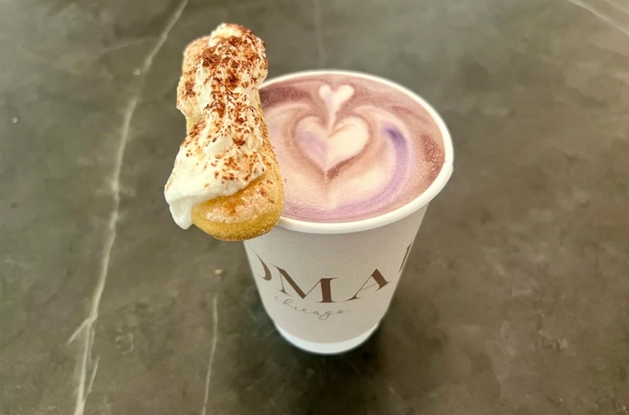 Purple coffee latte with the foam in the shape of a heart with a cookie with whipped cream on the side of the cup.