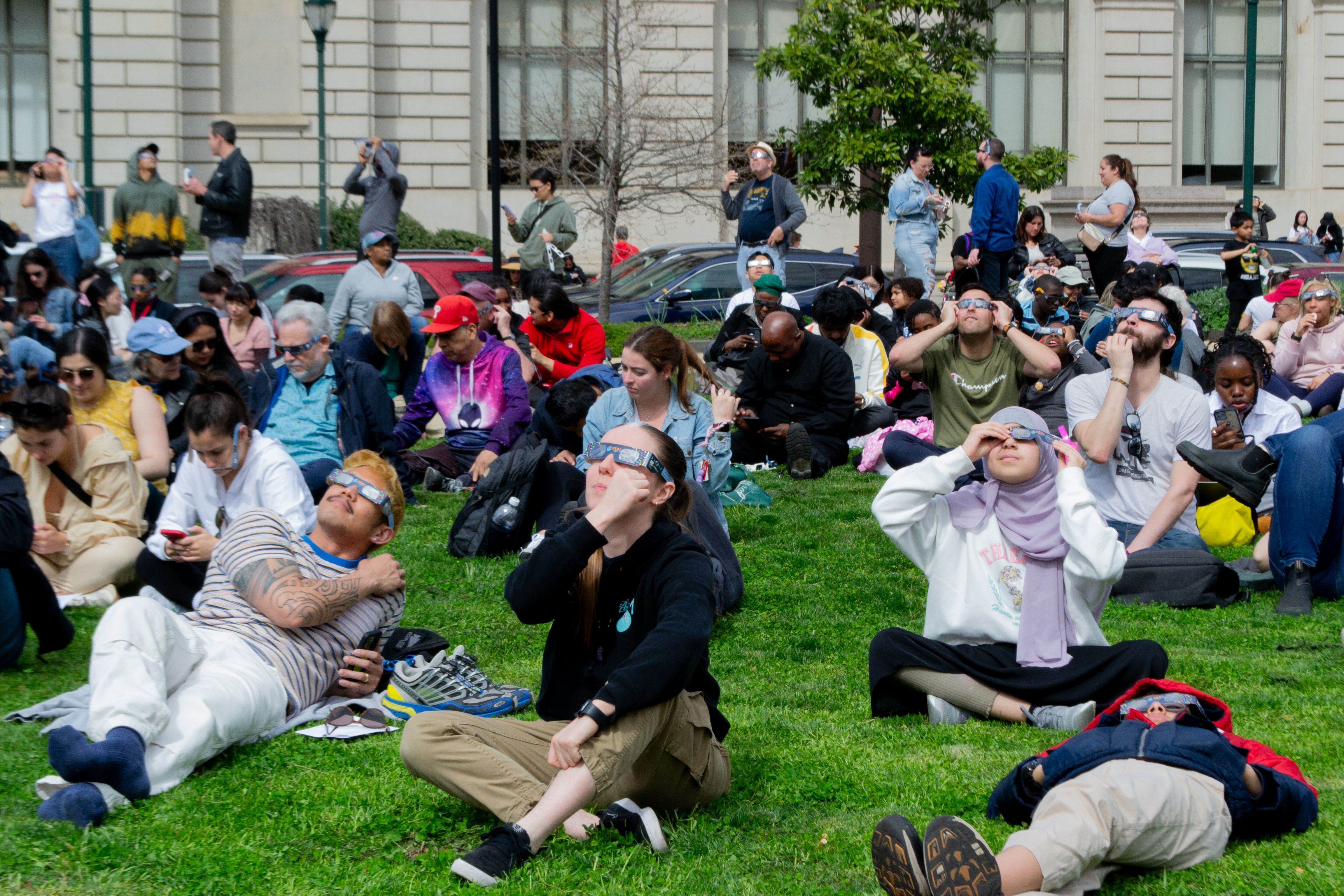 A crowd of people wearing eclipse glasses sitting down.
