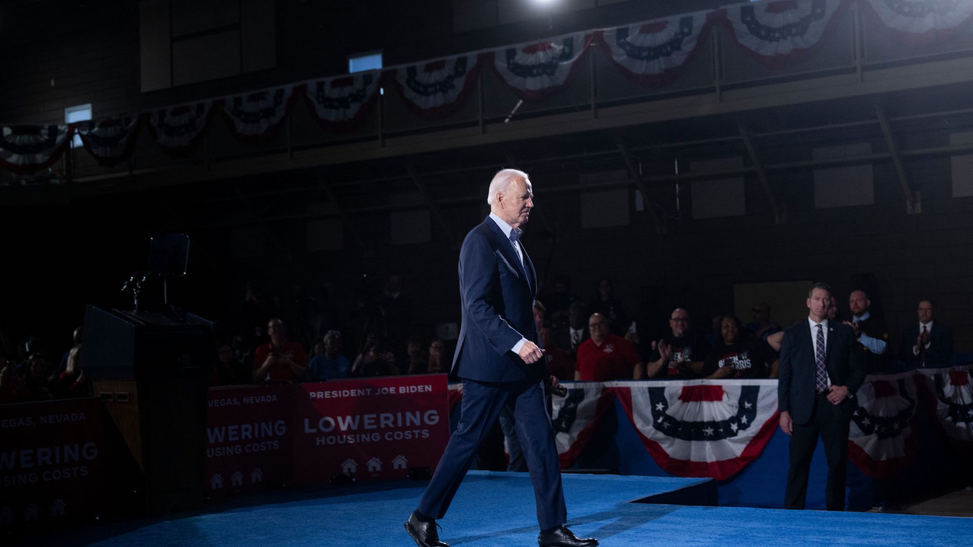 President Biden walks across a blue carpet at a campaign rally.