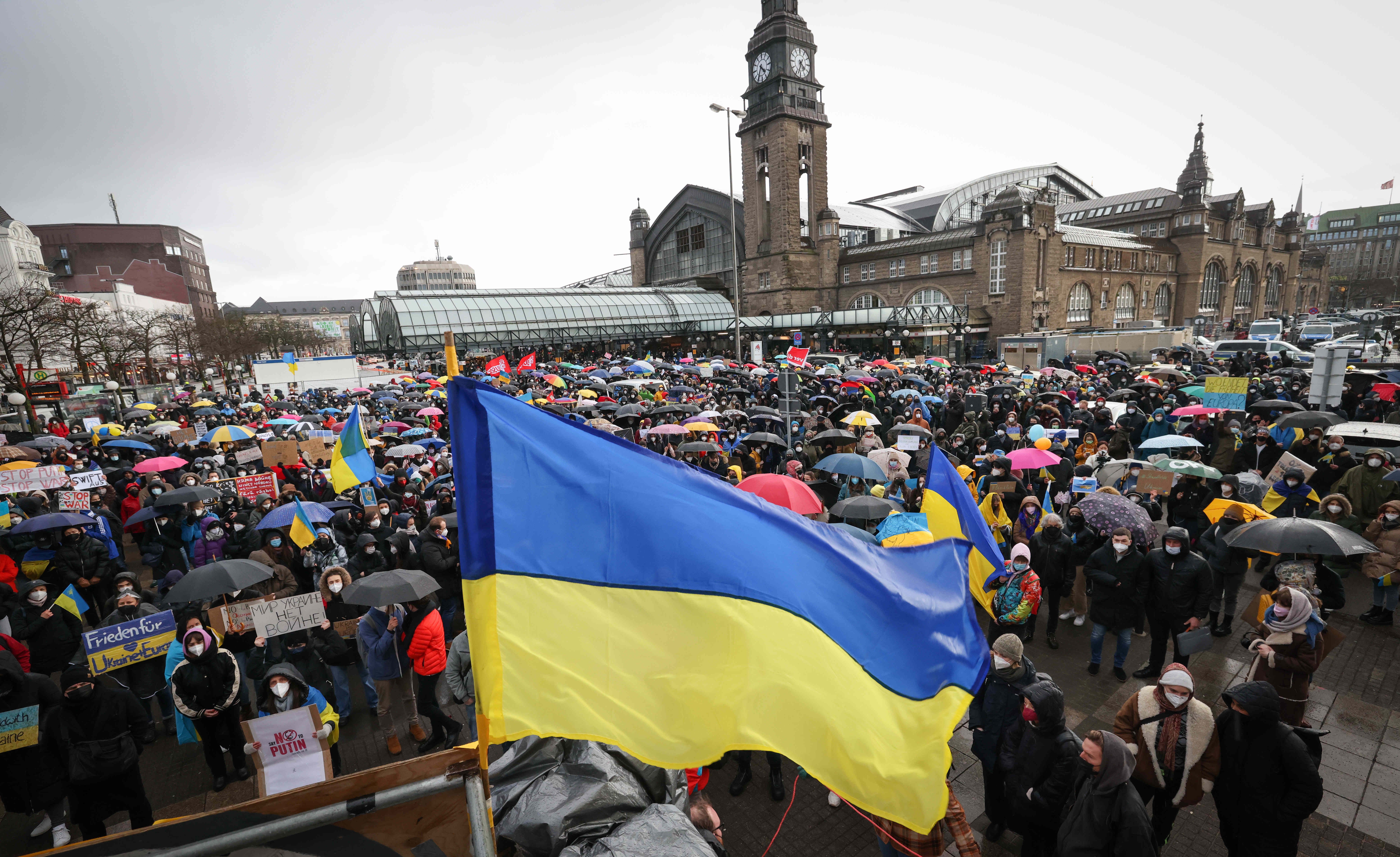 Photo of people holding umbrellas in the rain as a Ukraine flag is waved overhead