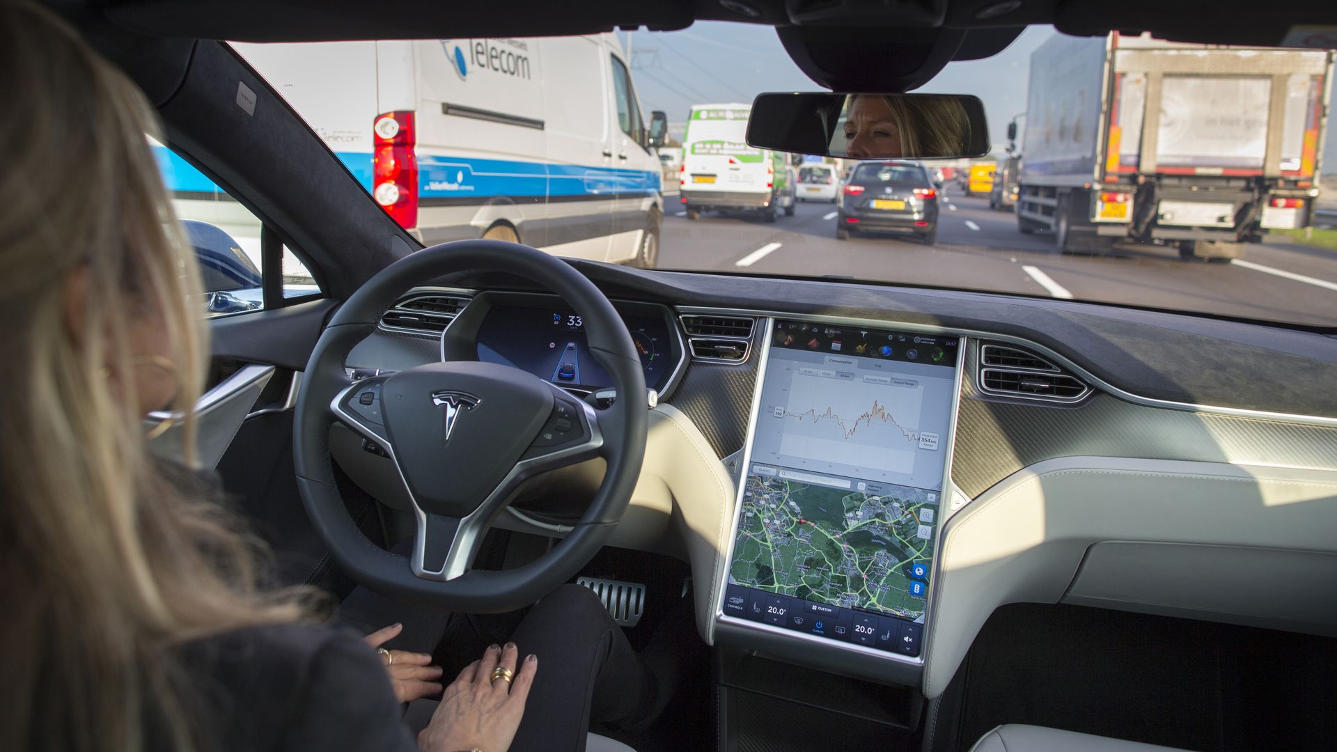 Image of a woman driving in a Tesla on the highway with her hands in her lap