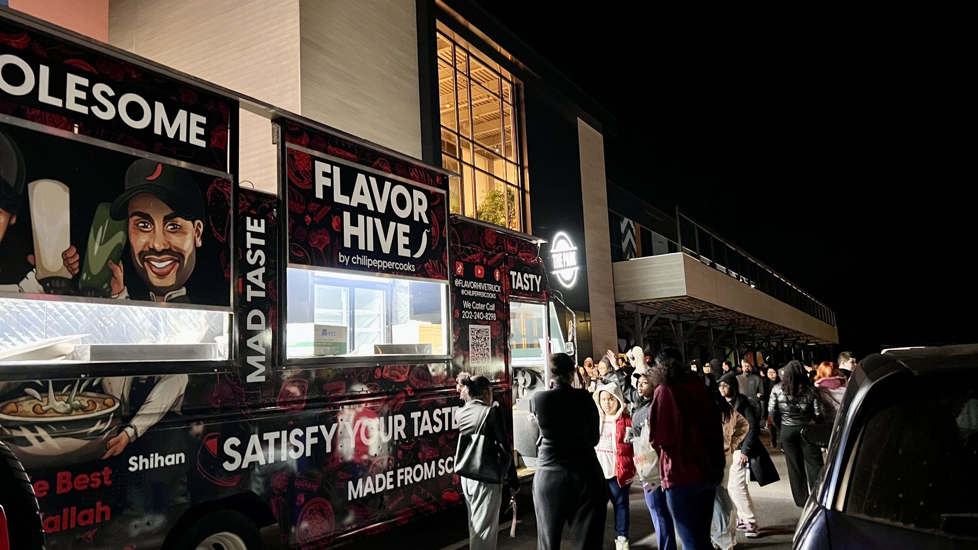 Night scene of a crowd waiting at the black and red Flavor Hive food truck with cartoon faces and text "Satisfy Your Taste" outside a lit building with a balcony.