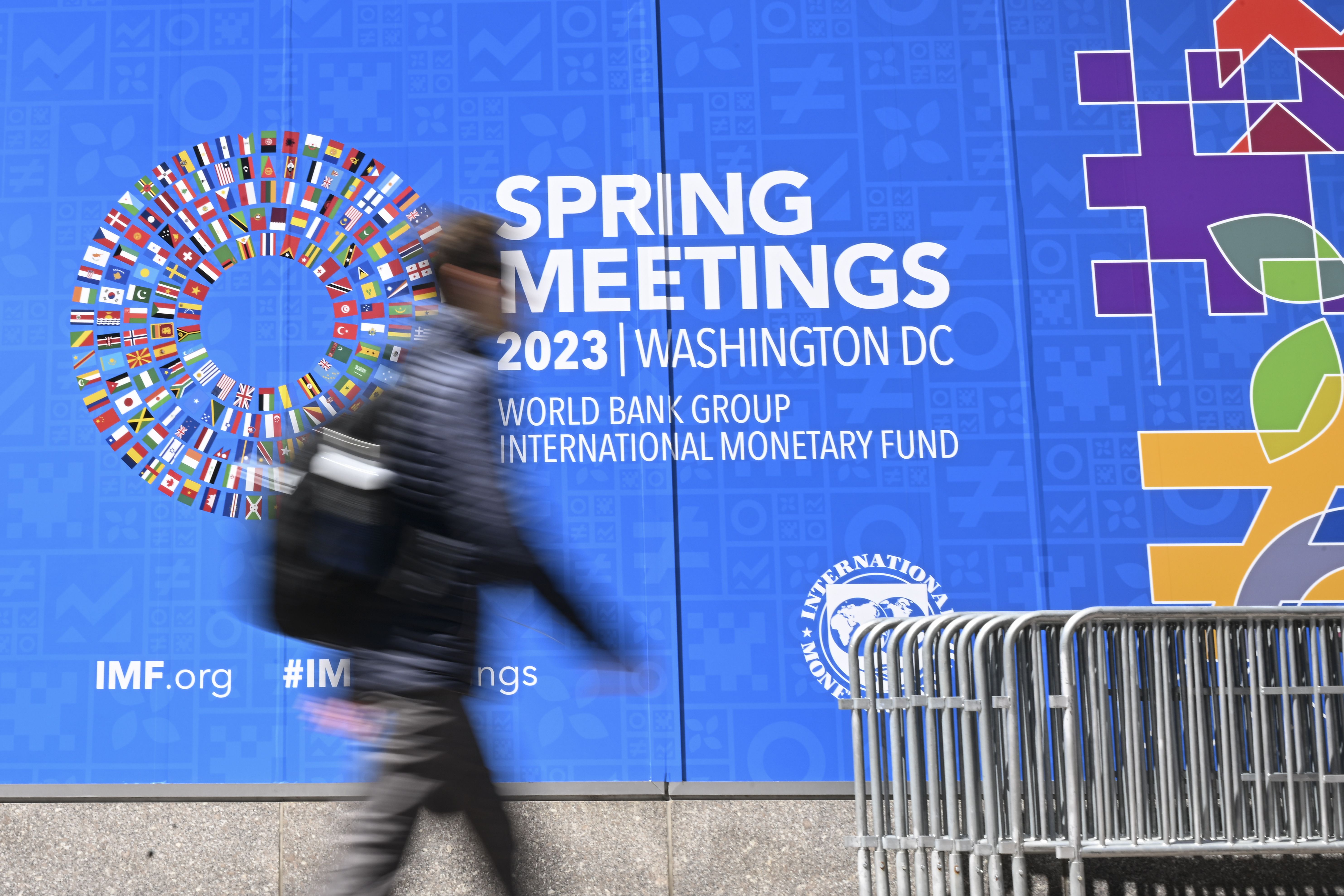 A person walks past a sign for the 2023 Spring Meetings of the World Bank/International Monetary Fund in Washington D.C.