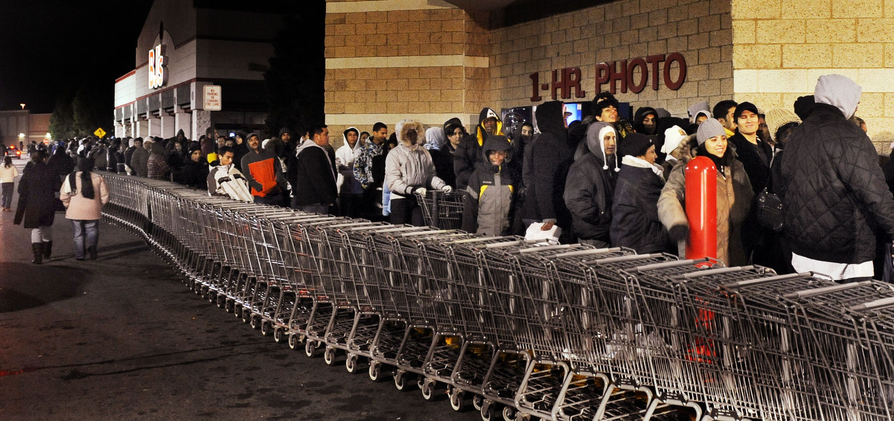 People waiting in line outside a store in the middle of the night next to a line of shopping carts.
